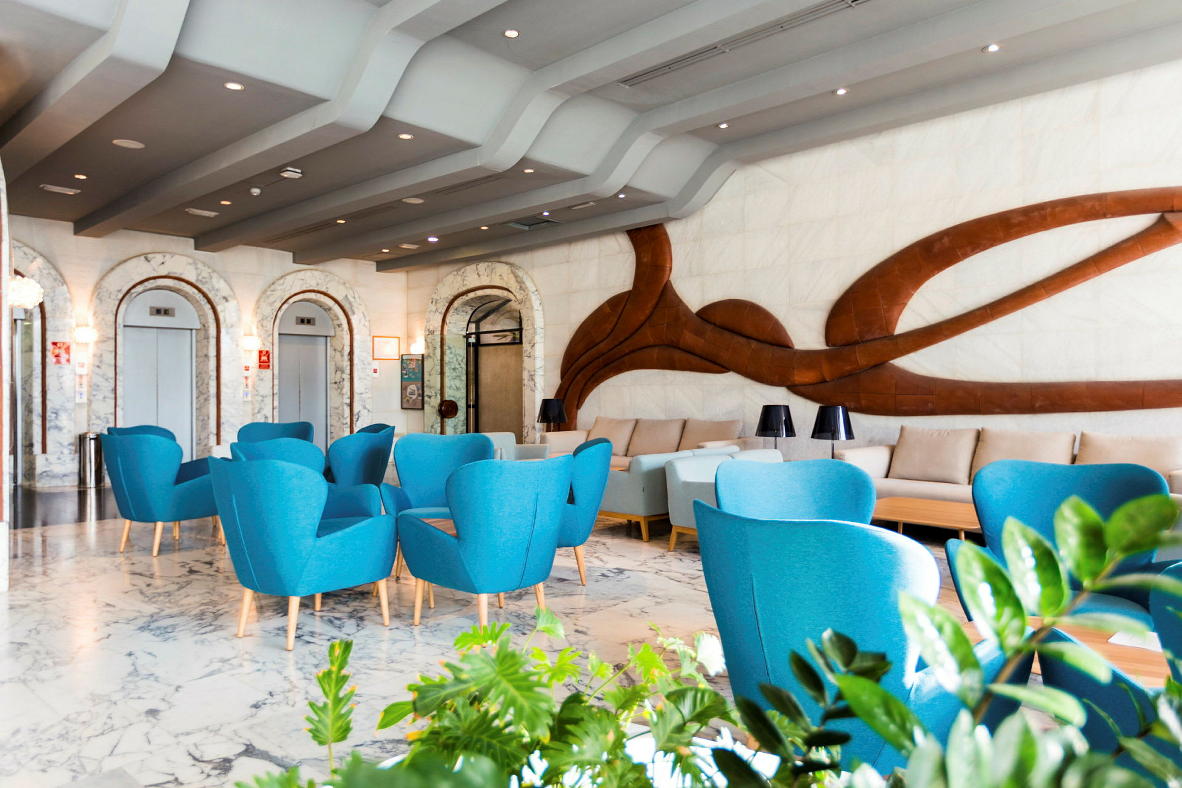 Moderne hotellobby med blå lænestole og dekorativ væg. (AI-genereret tekst)