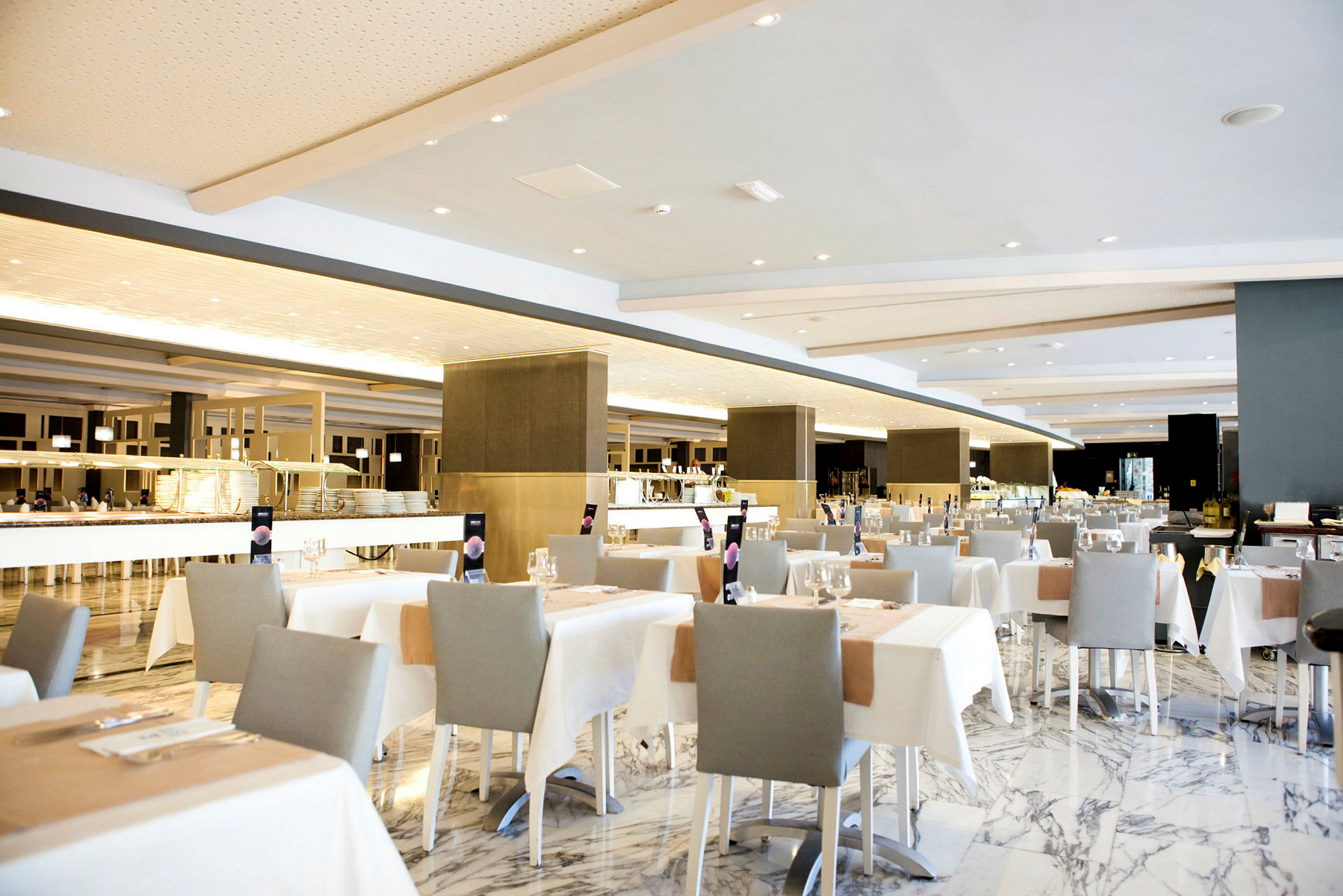 En rummelig restaurant med elegant opstillede borde, hvide duge og grå stole. (AI-genereret tekst)
