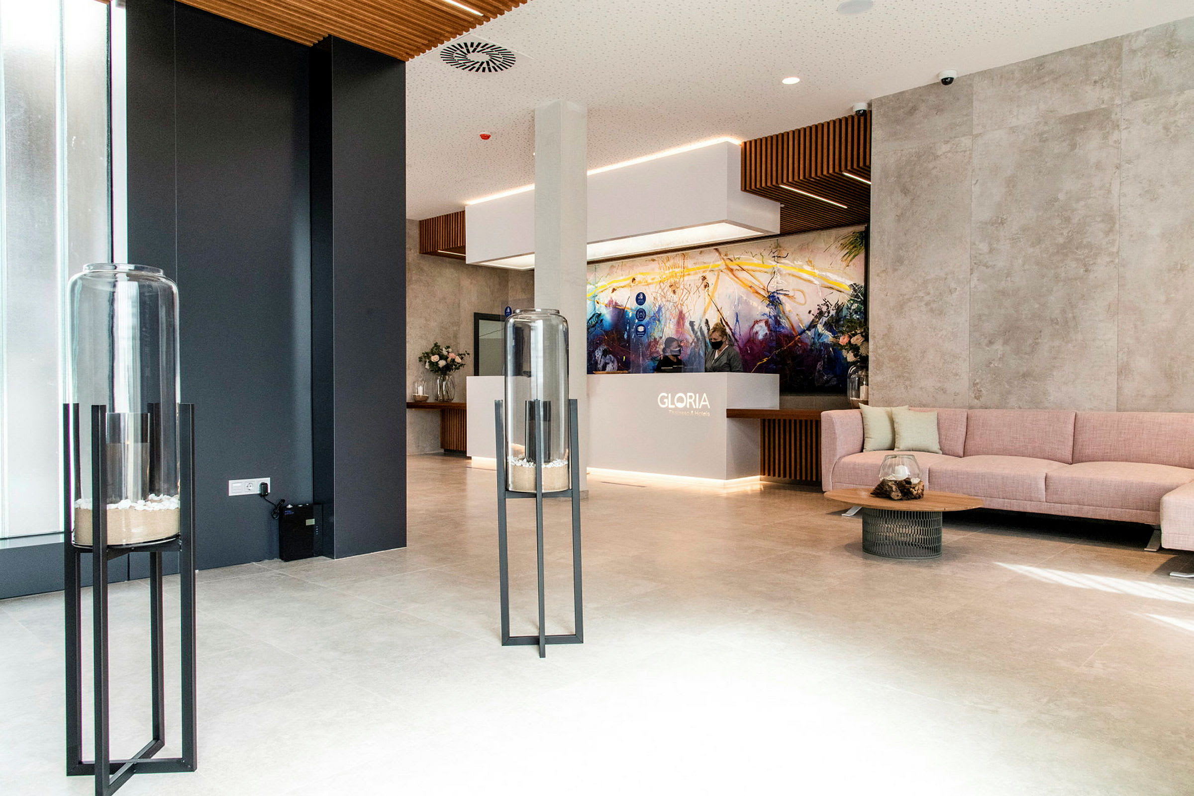 Moderne hotellobby med receptionen mærket 'Gloria', sidemøbler og dekorative elementer såsom glasbeholdere på stativer. (AI-genereret tekst)