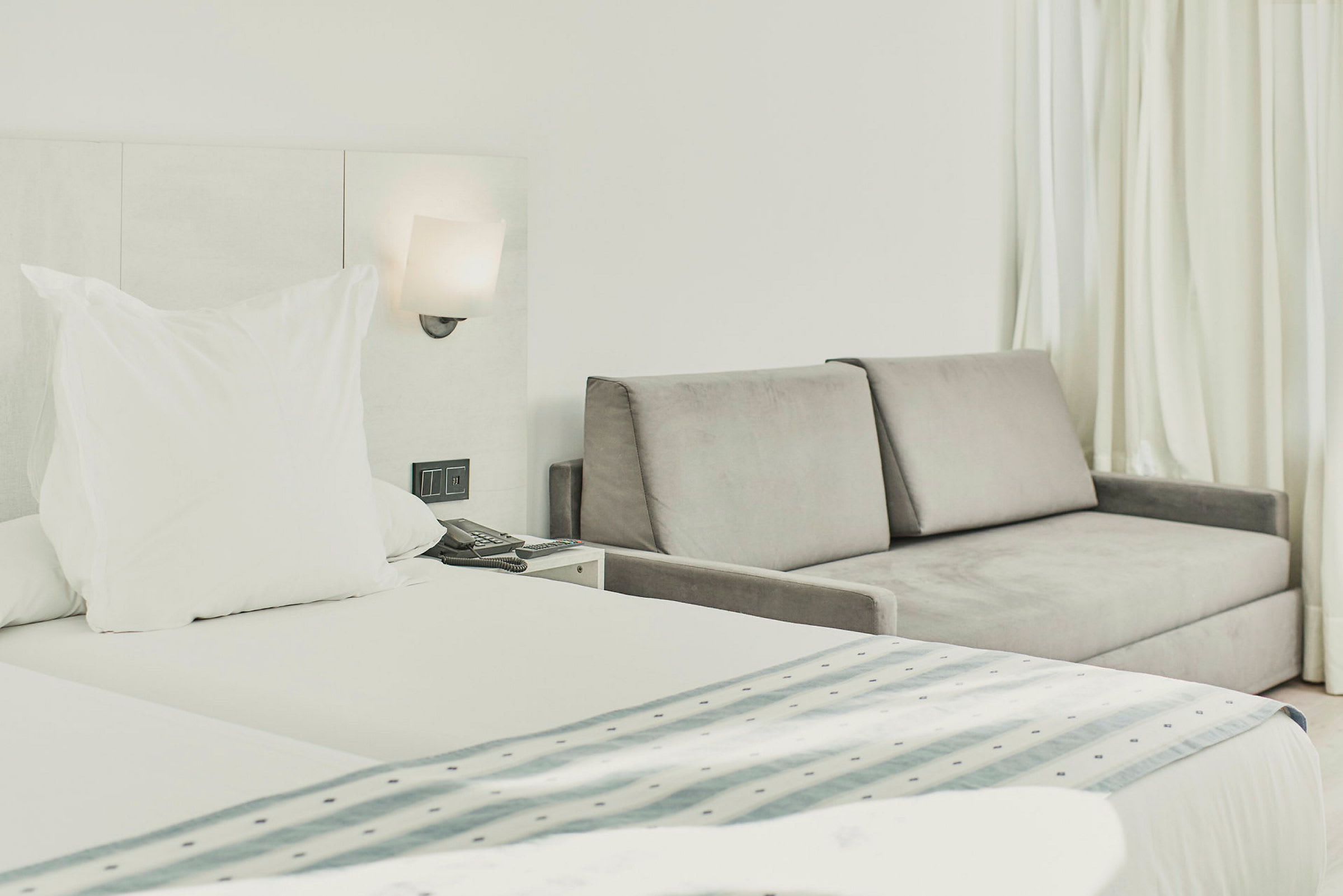 Hotelværelse med seng og grå sofa ved siden af. (AI-genereret tekst)