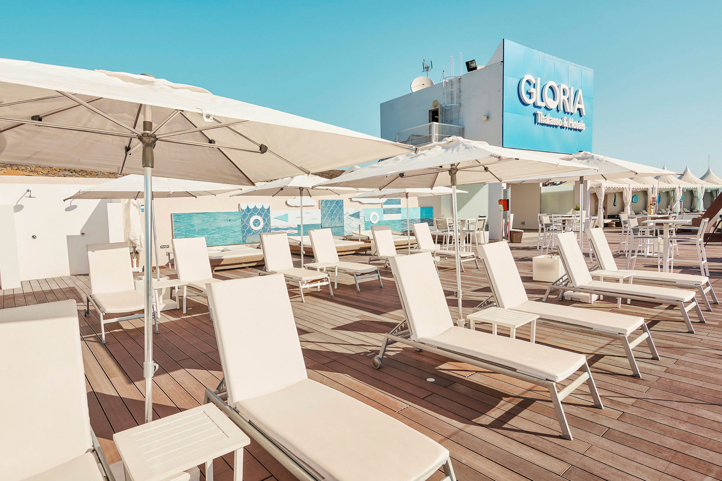 Liggestole og parasoller på terrasse med hotellets skilt i baggrunden. (AI-genereret tekst)