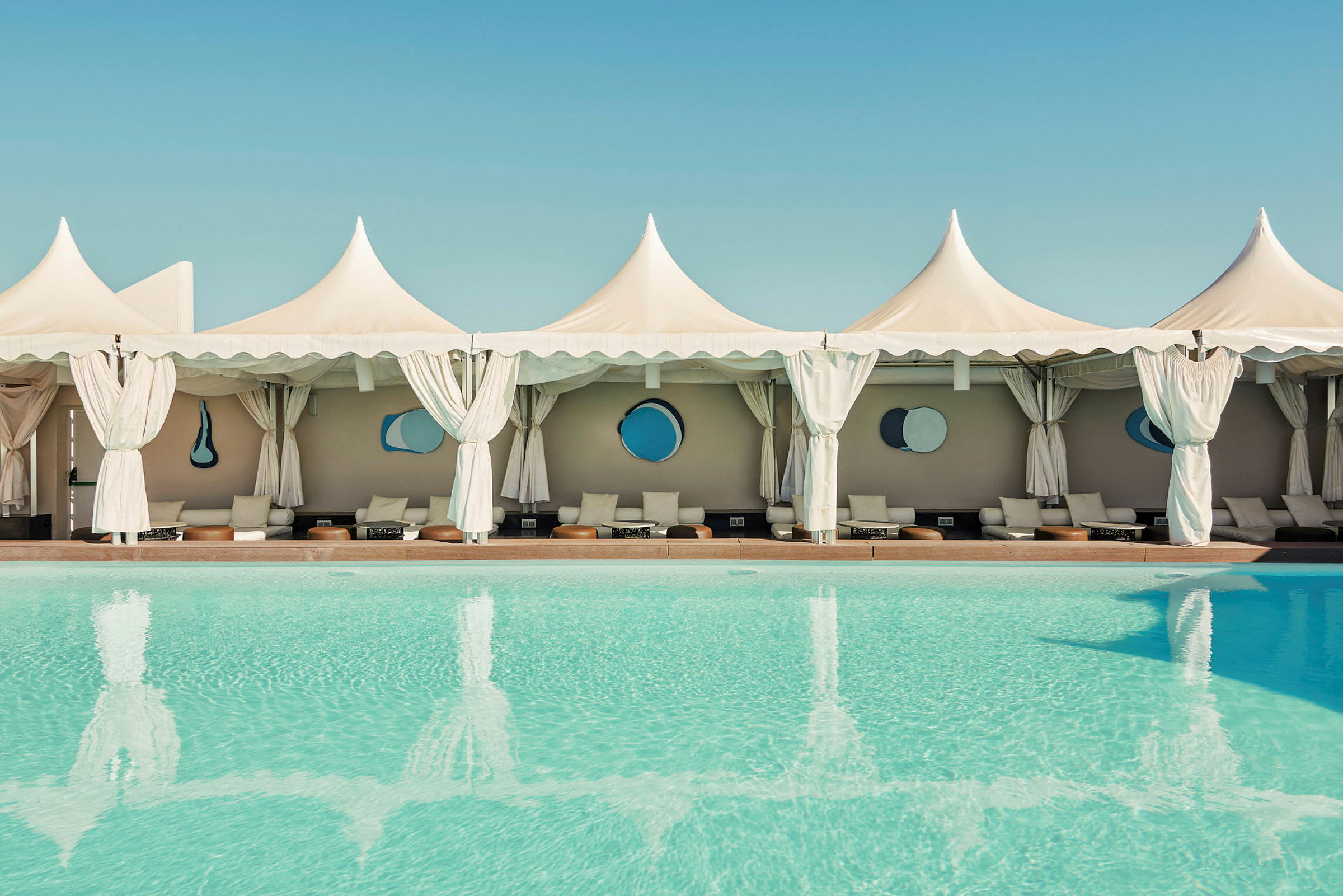 Swimmingpool med cabanas og hvide telte i baggrunden. (AI-genereret tekst)
