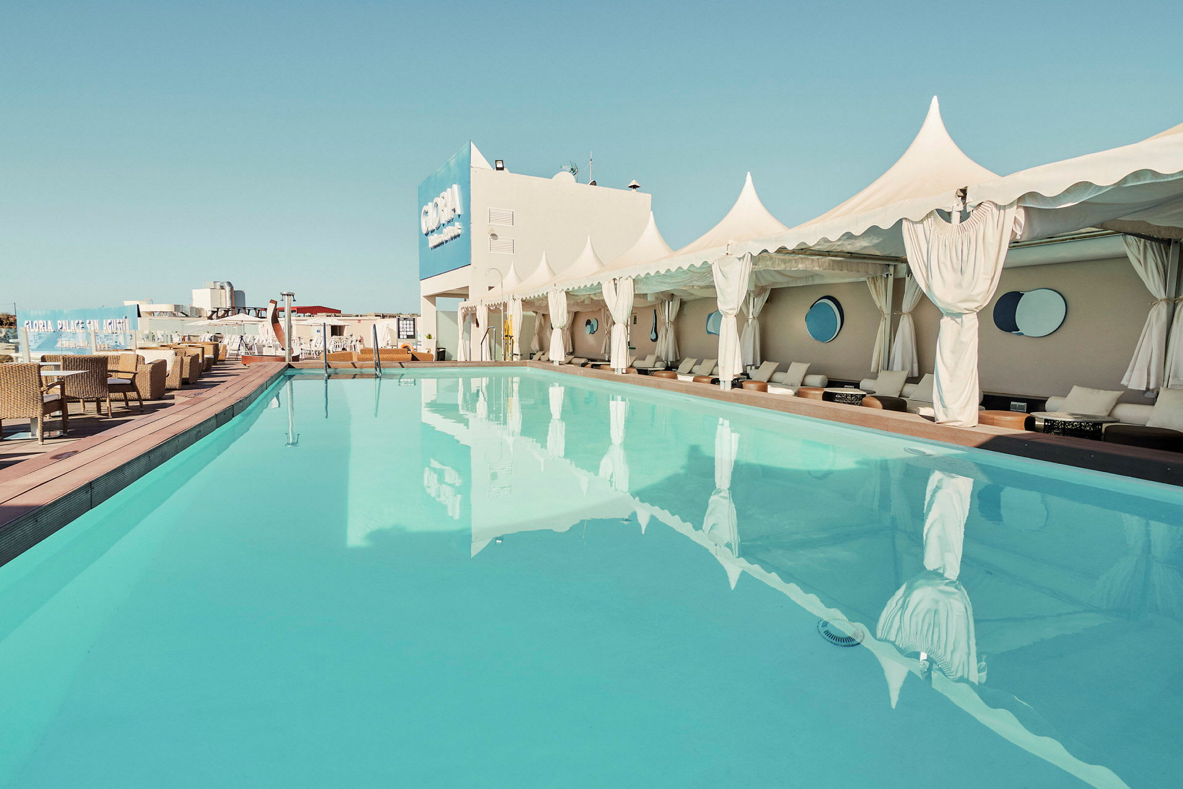 En udendørs terrasse ved en pool med liggestole og møbler under teltlignende baldakiner. (AI-genereret tekst)