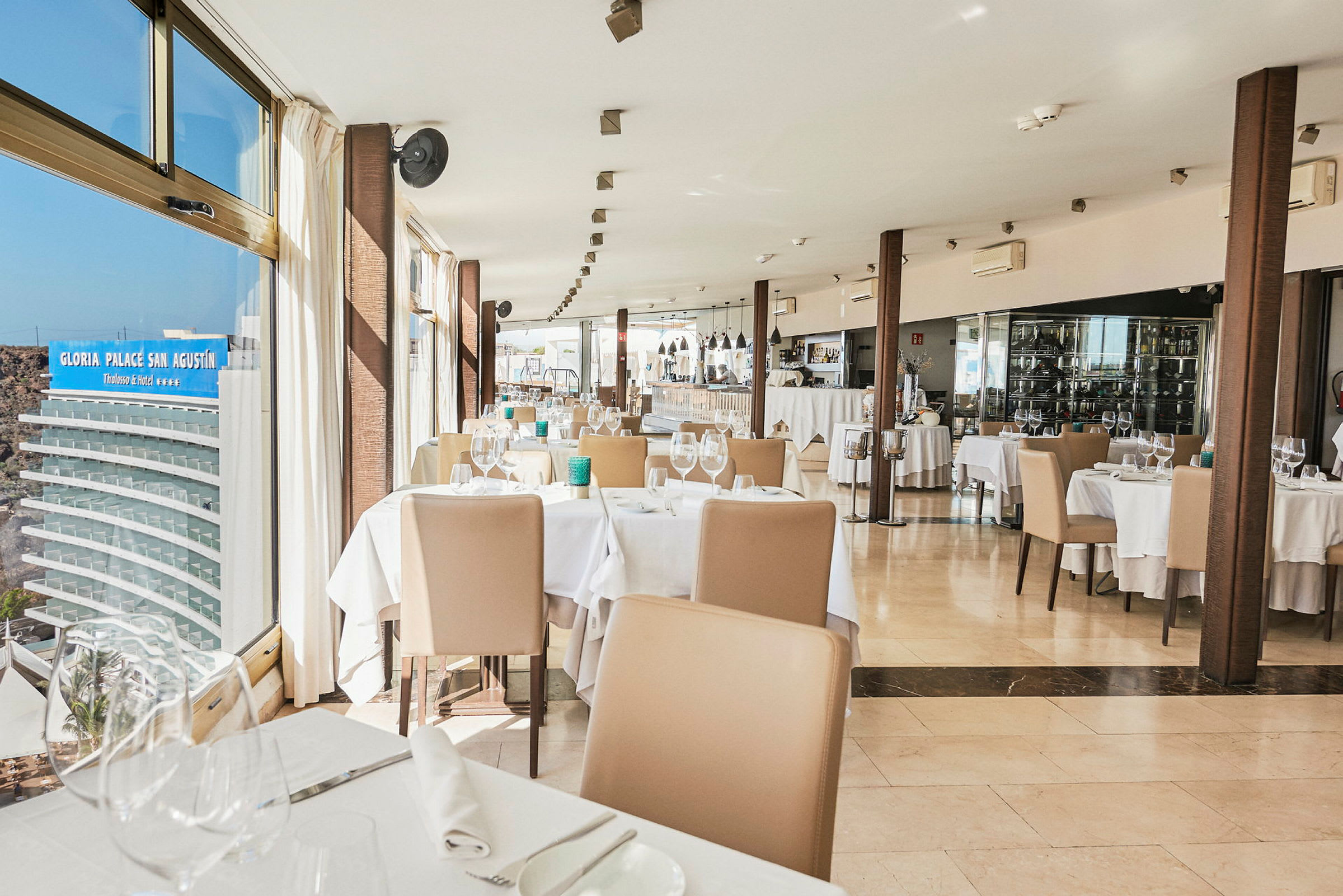 Billede af en restaurant med dækkede borde og stole ved siden af store vinduer. (AI-genereret tekst)