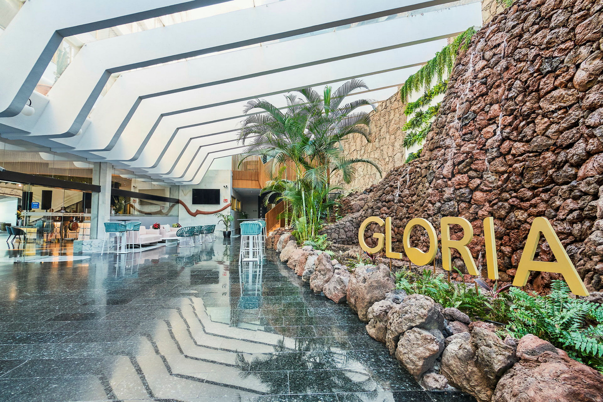 Hotellobby med stenmur, planter og teksten Gloria. (AI-genereret tekst)