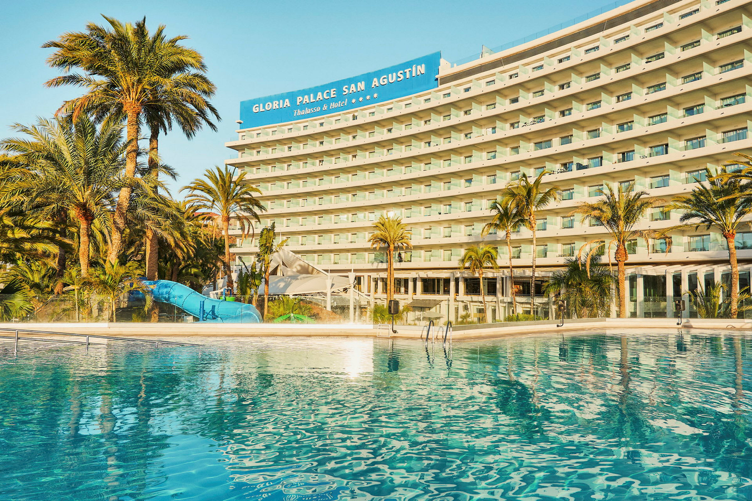 Et hotel med en pool og palmer i forgrunden. (AI-genereret tekst)