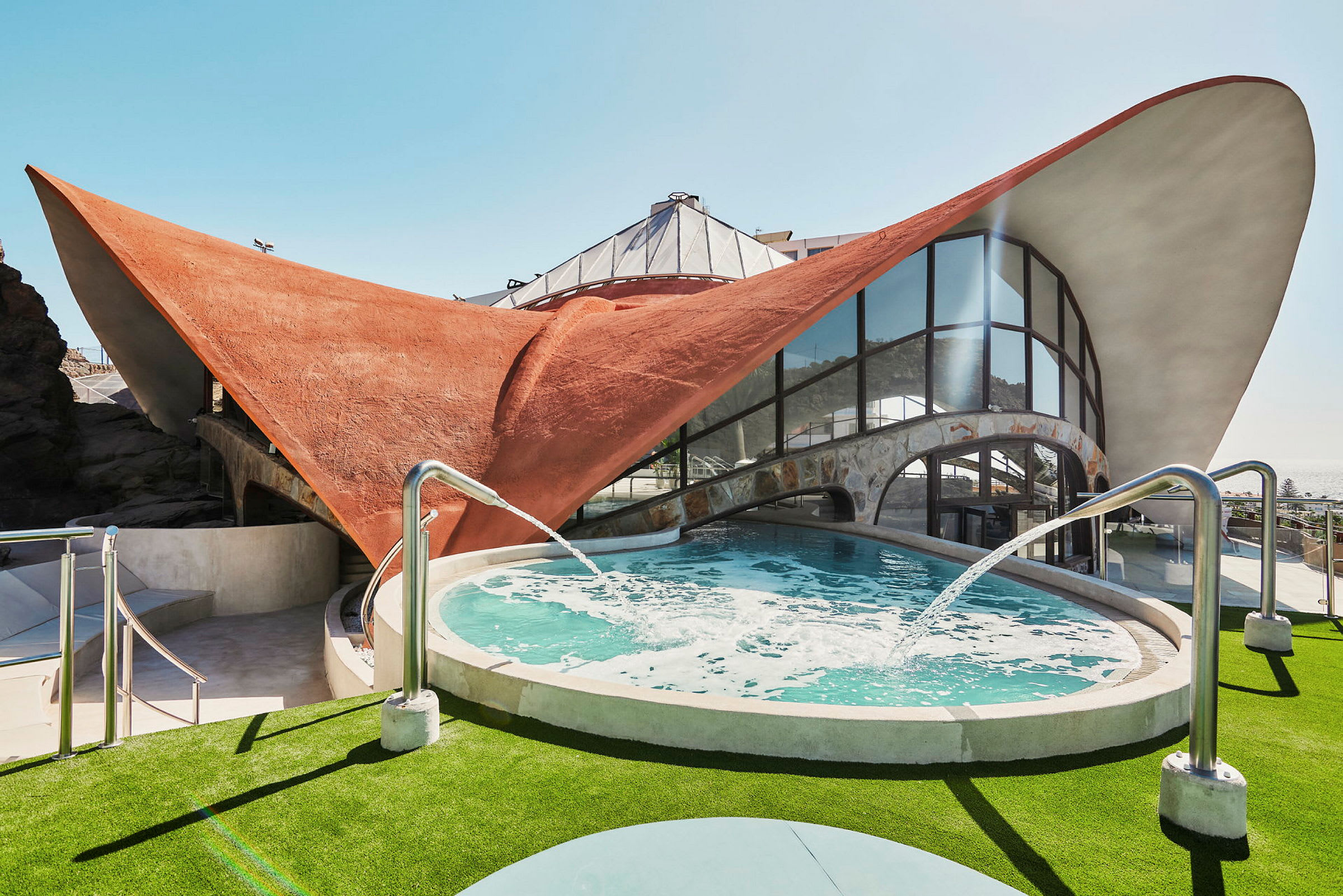 Udendørs pool med vandstrømme og en bygning i moderne arkitektur. (AI-genereret tekst)