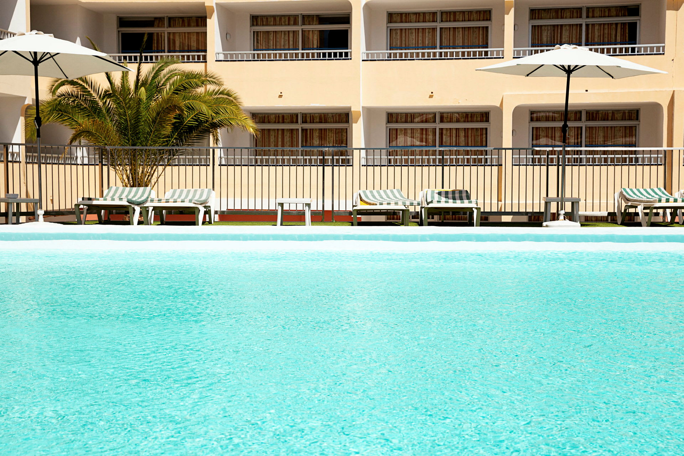 Udendørs swimmingpool med liggestole og parasoller i baggrunden. (AI-genereret tekst)
