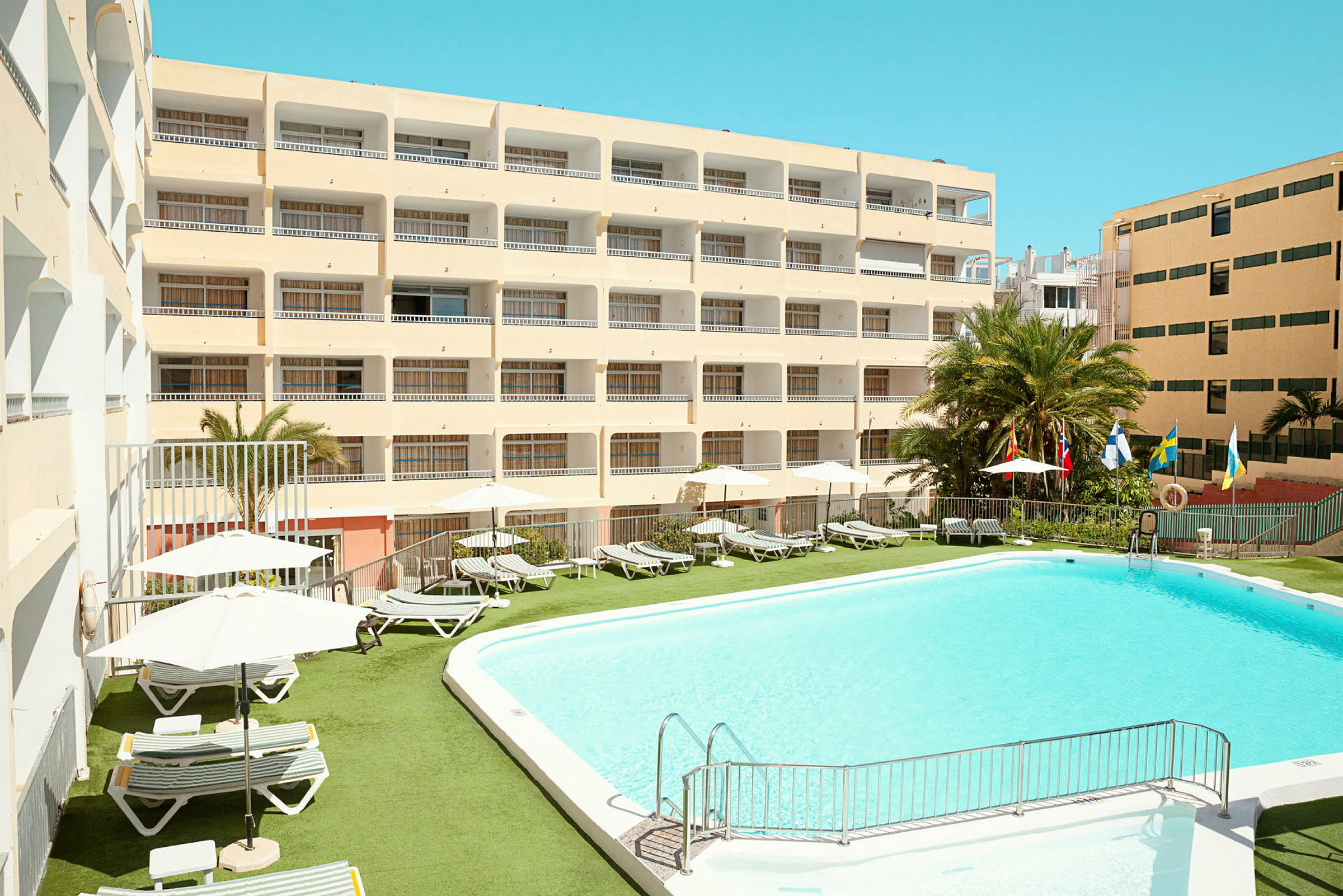 Hotelbygning med swimmingpool og liggestole udendørs. (AI-genereret tekst)