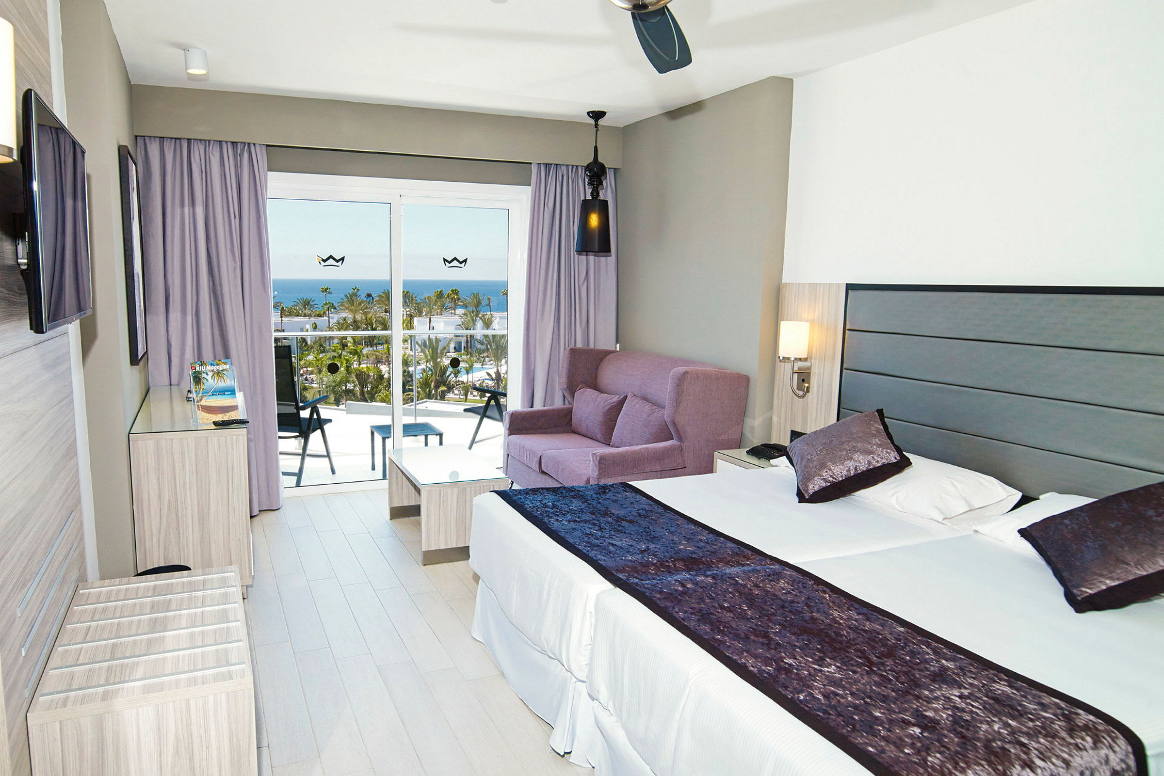 Moderne hotelværelse med en dobbeltseng, sofagruppe og altan med udsigt over havet. (AI-genereret tekst)