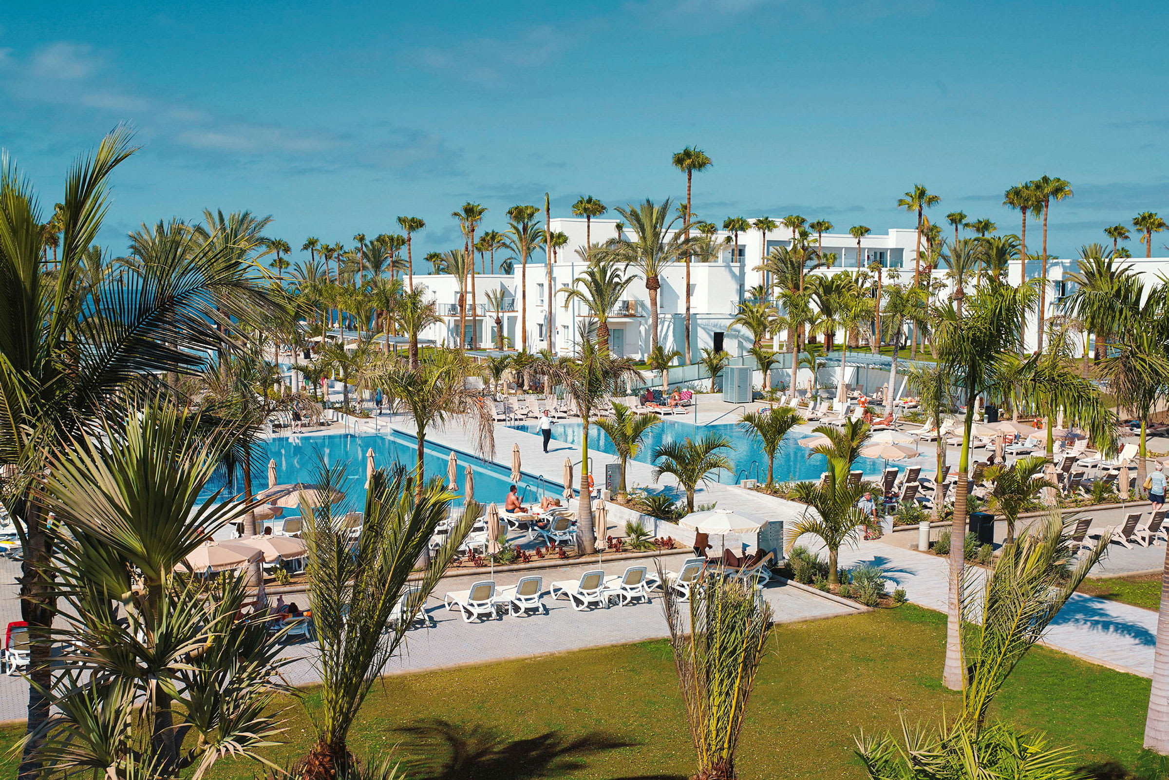 Hotelområde med hvide bygninger, swimmingpools og palmer. (AI-genereret tekst)