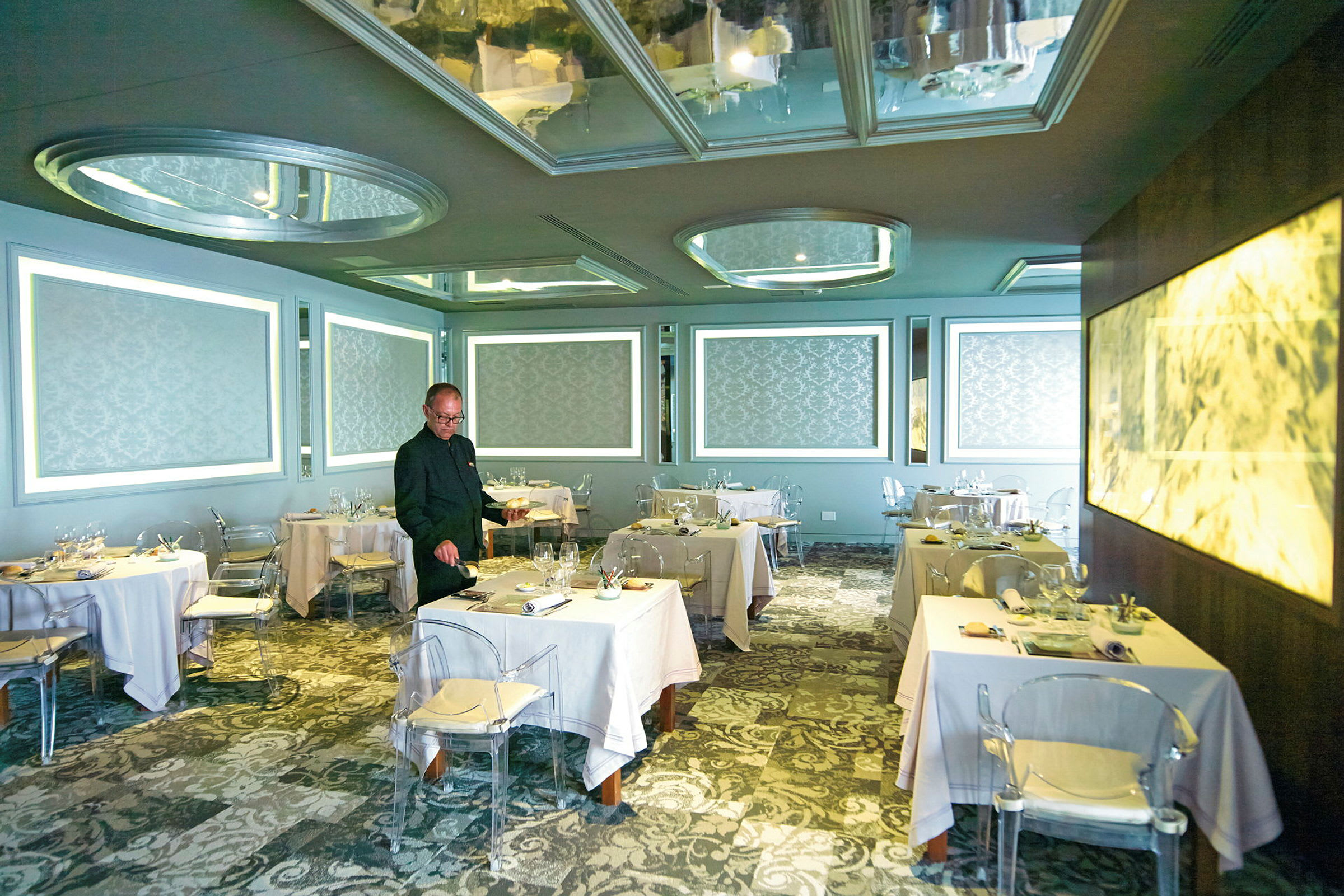 En elegant restaurant med borde dækket med hvide duge, mønstrede vægge og moderne lysinstallationer. (AI-genereret tekst)