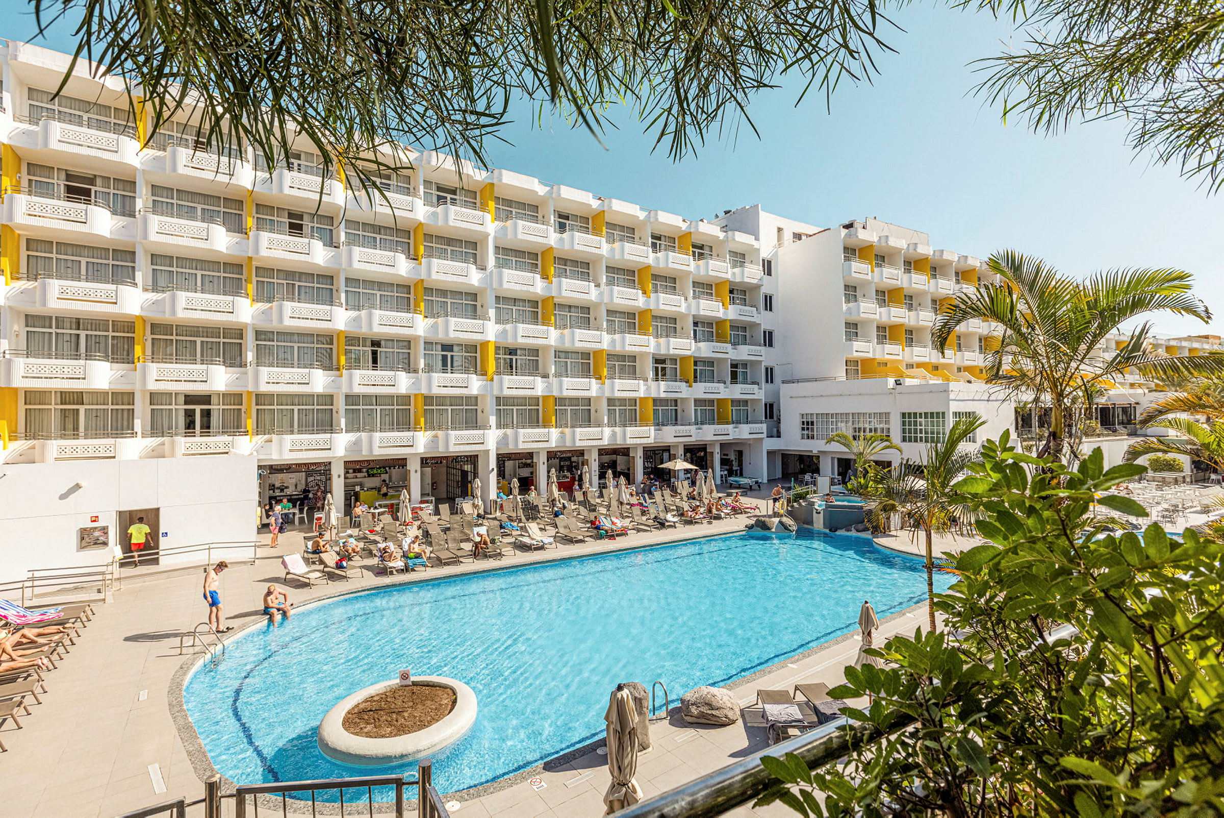 Hotelbygning med flere etager og en stor pool foran. (AI-genereret tekst)