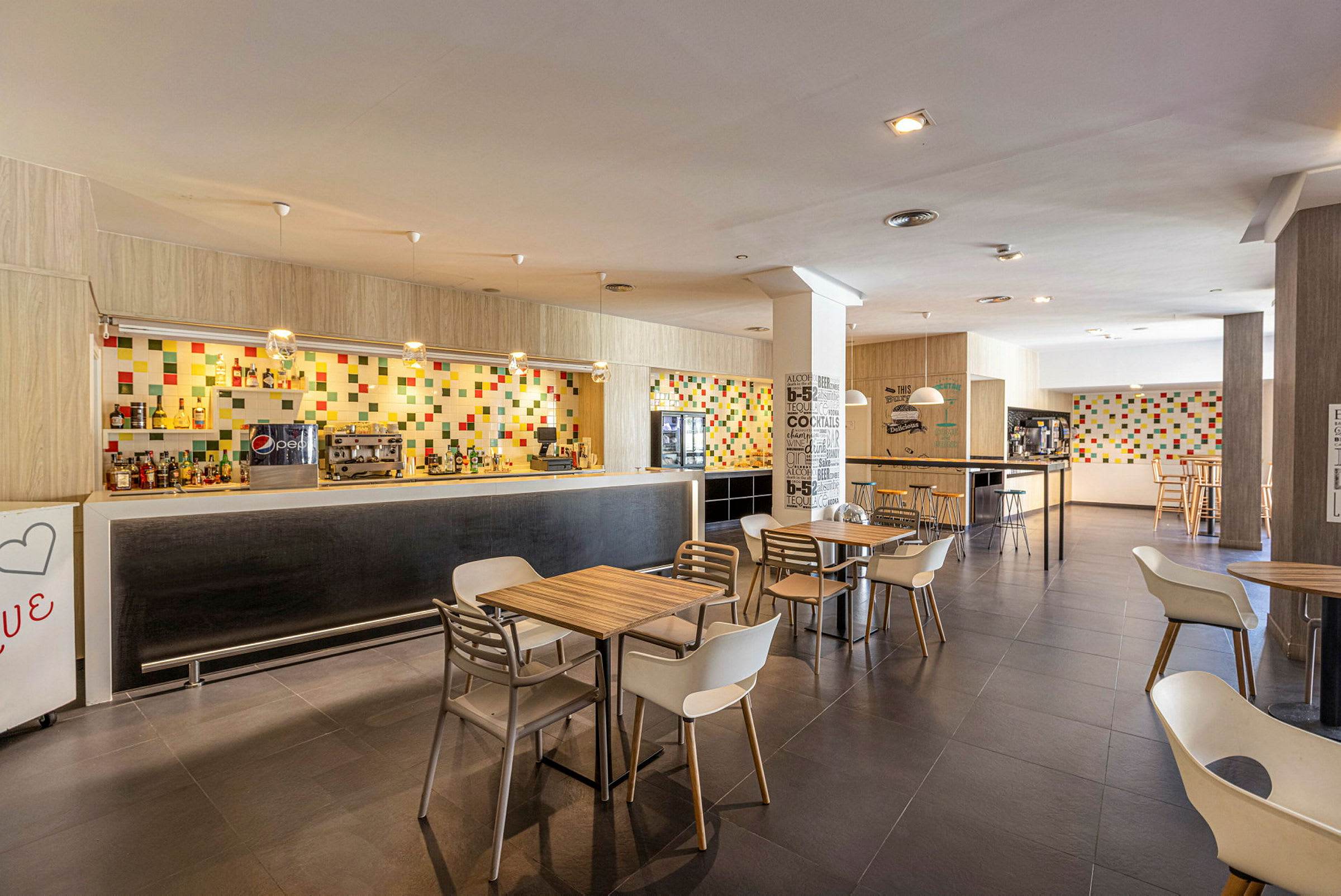 Moderne café- og bardesign med farverig flisevæg og møblerede borde og stole. (AI-genereret tekst)