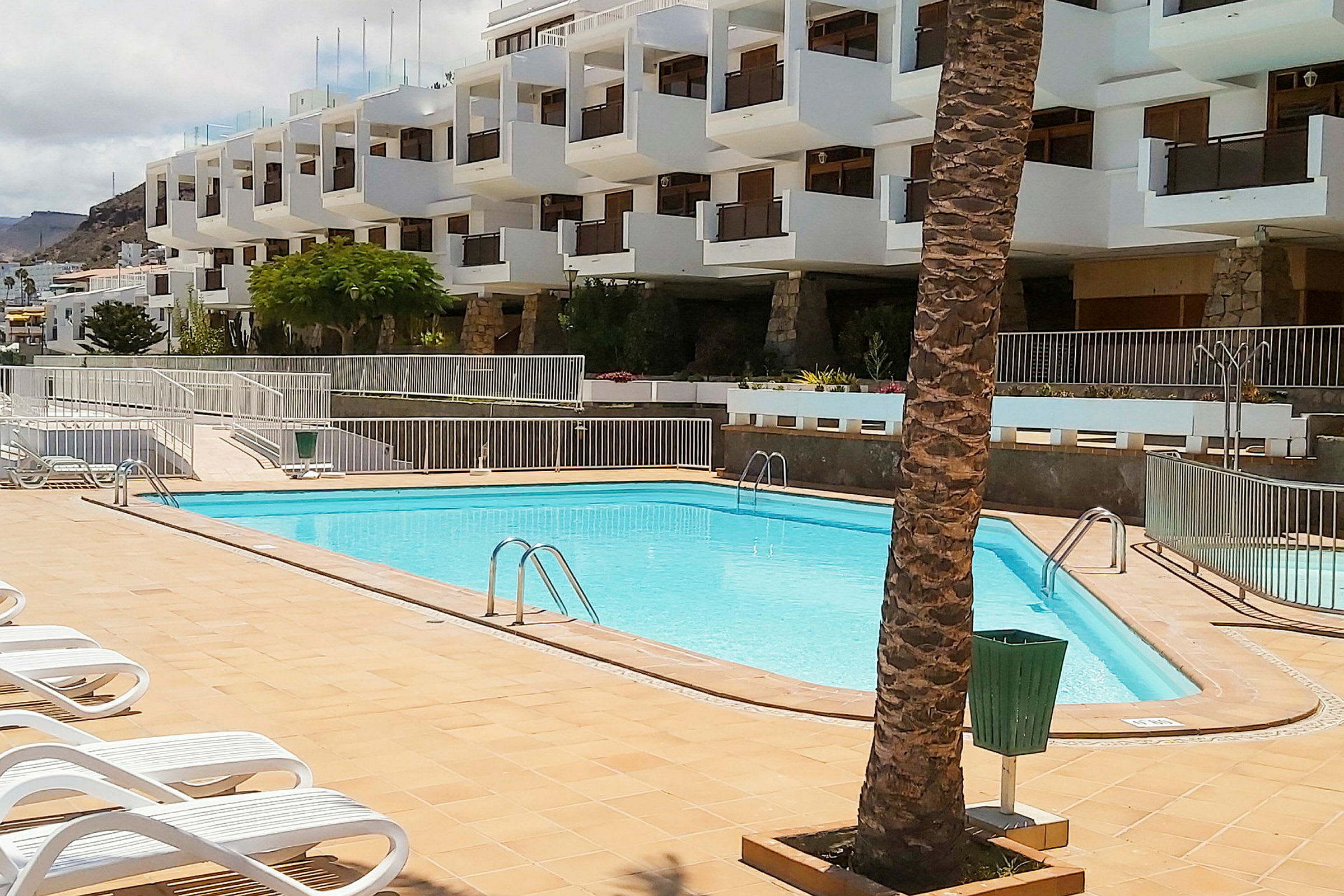 Pool med liggestole foran en hvid bygning. (AI-genereret tekst)