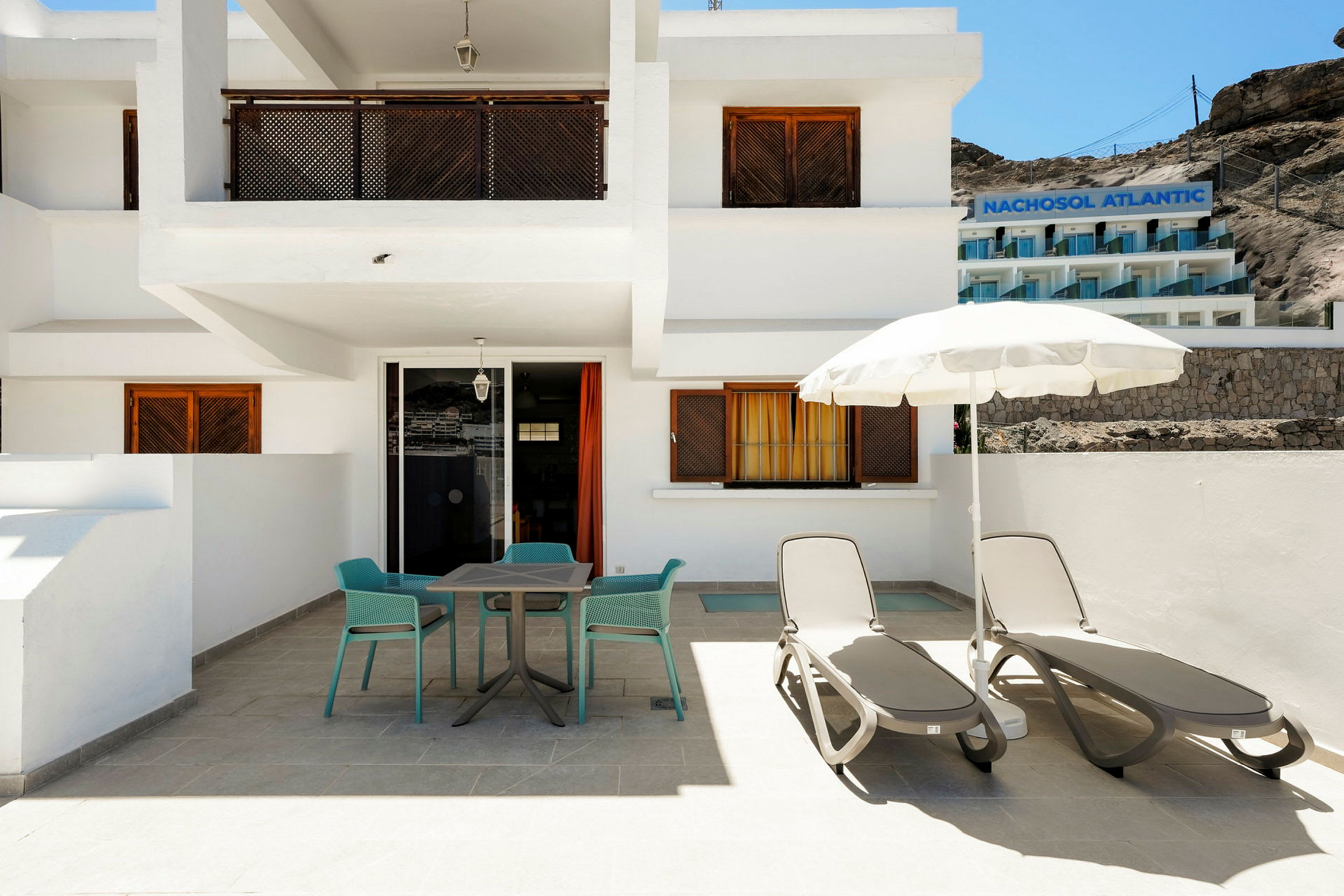 Hotelfacade med en terrasse med liggestole og parasol. (AI-genereret tekst)