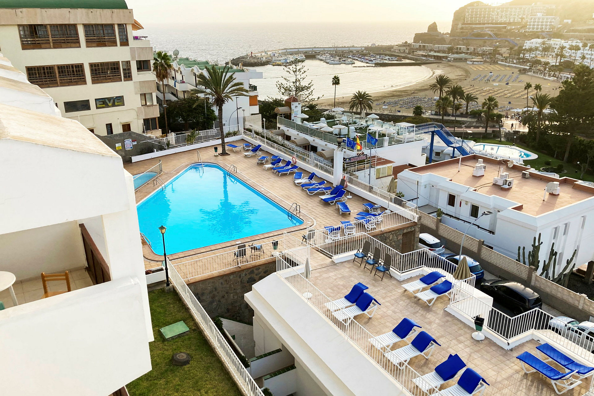 Udsigt over en hotelpool og liggestole med havet i baggrunden. (AI-genereret tekst)