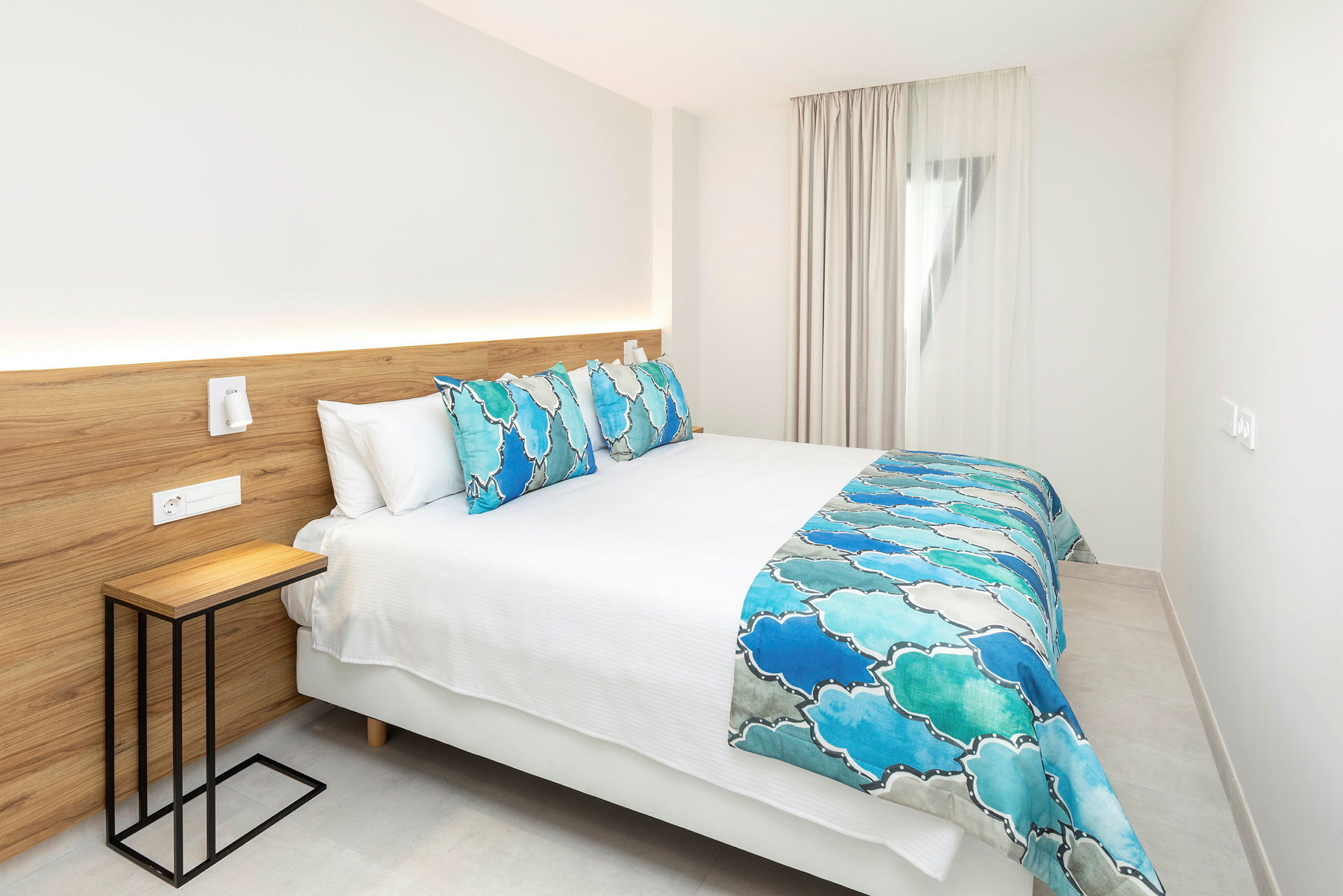 Moderne hotelværelse med en dobbeltseng med blå og hvide sengetæpper. (AI-genereret tekst)