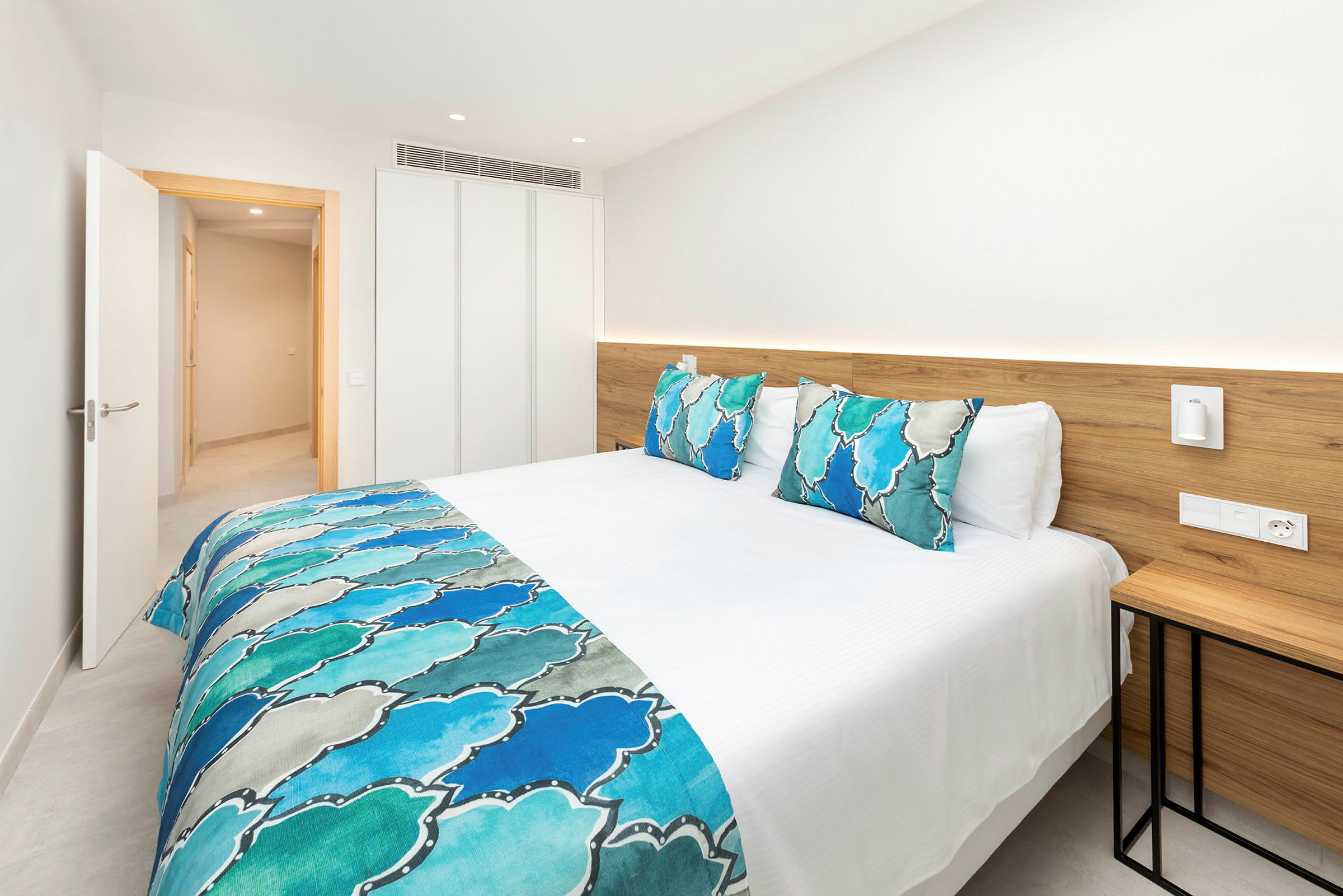 Seng med hvidt sengetøj og blå dekorative detaljer i et lyst hotelværelse. (AI-genereret tekst)