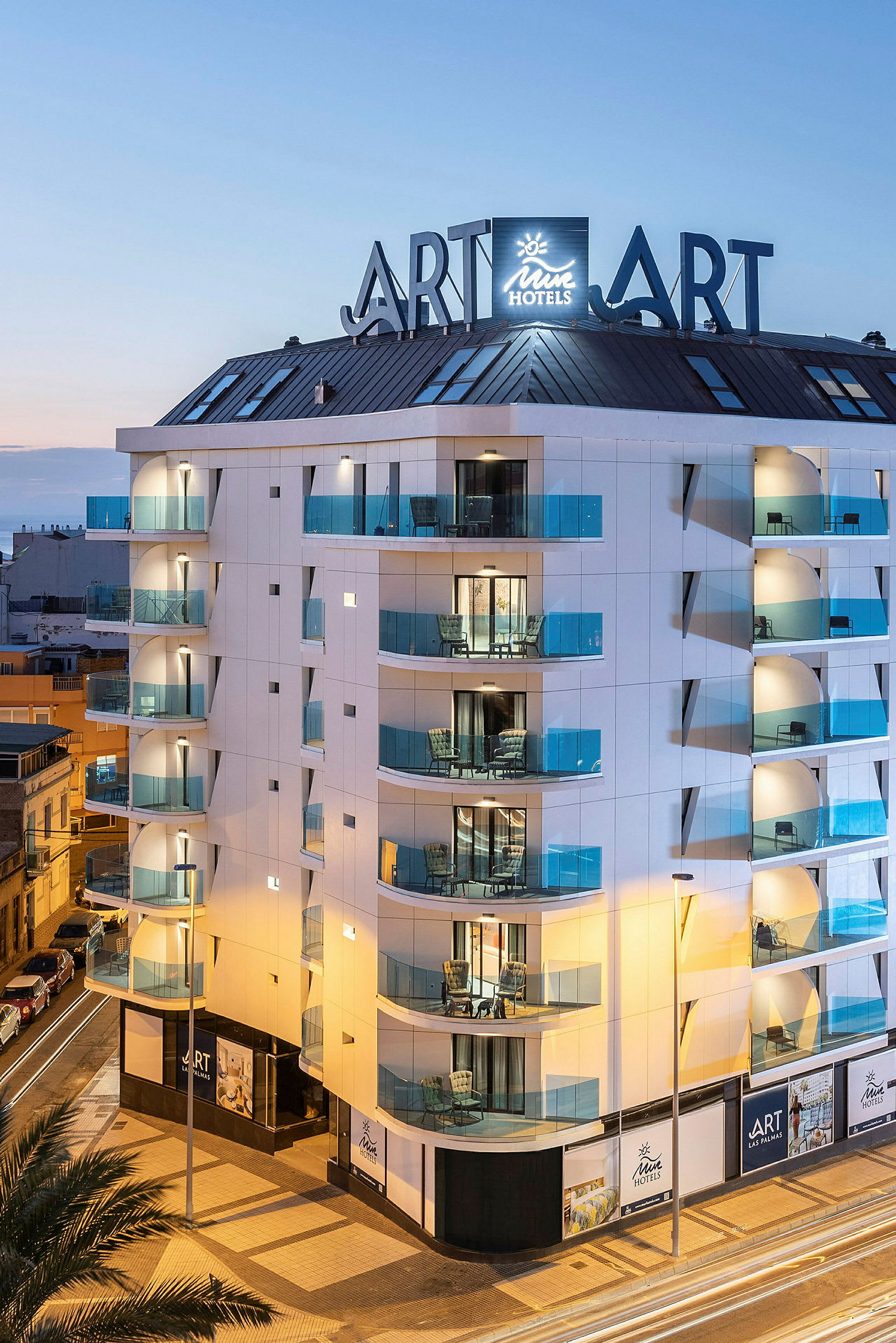 En moderne hotelbygning med glasbalkoner og skilte under en aftenshimmel. (AI-genereret tekst)