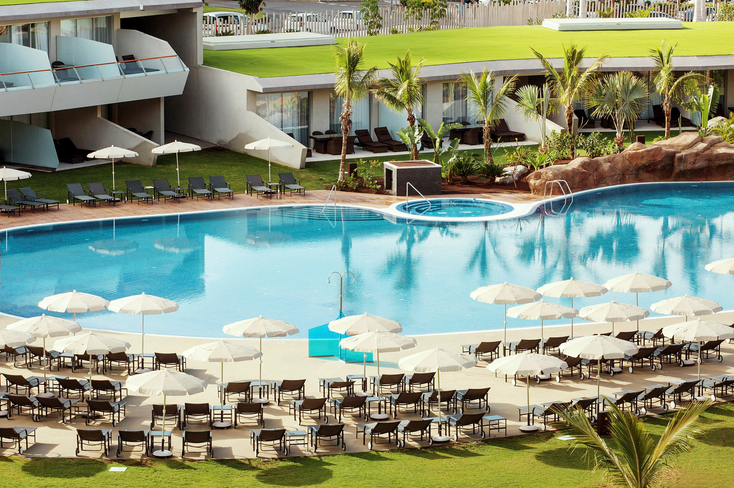 En hotelpool med liggestole og parasoller omkring. (AI-genereret tekst)