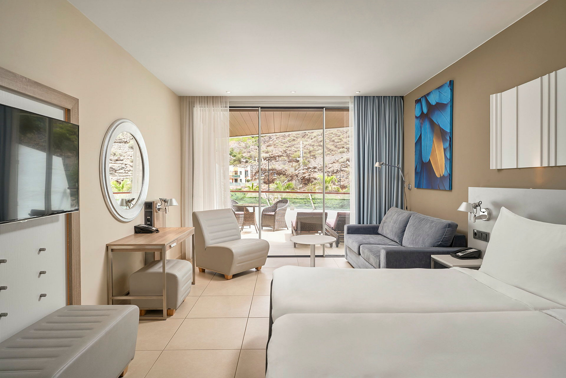 Hotelværelse med to enkeltsenge, sofa og sidde møbler. Glasdøre fører til en terrasse med udsigt. (AI-genereret tekst)