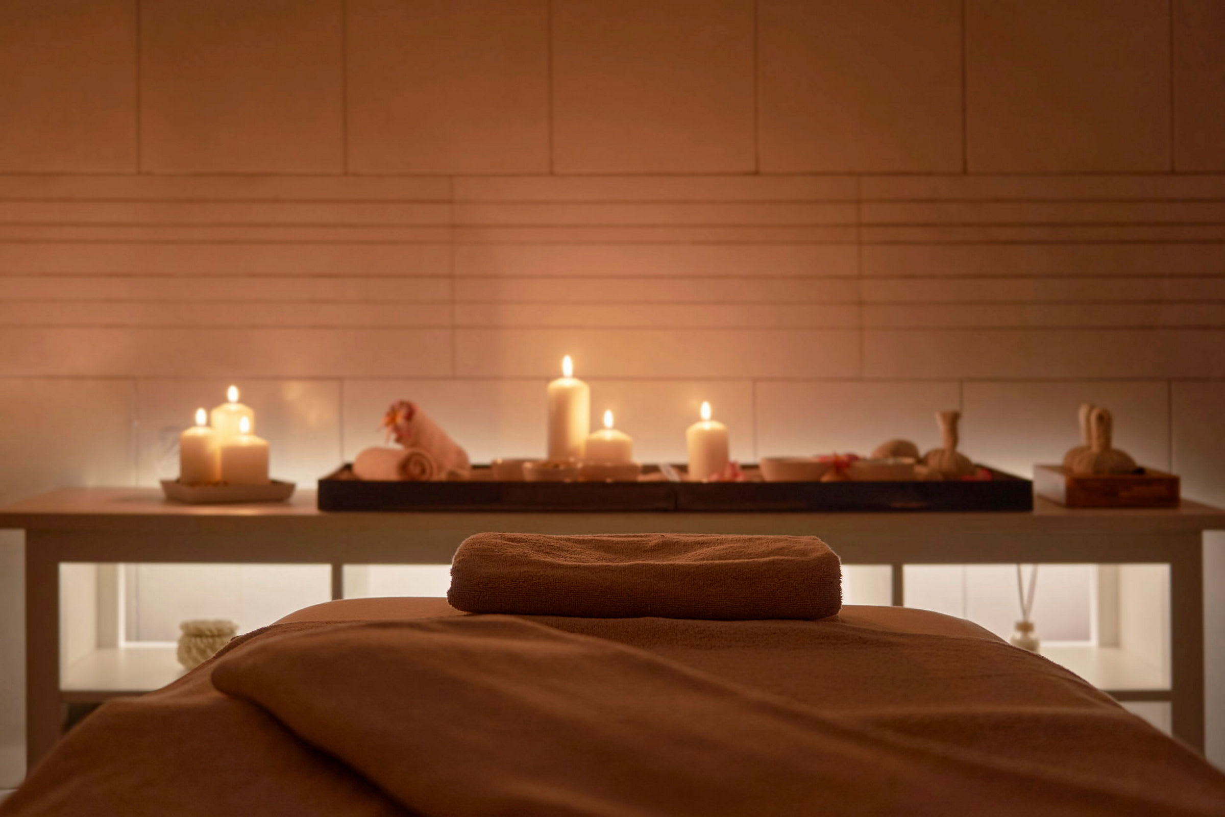 En massagebænk med et håndklæde, placeret i et spaområde med lys og dekorative genstande. (AI-genereret tekst)