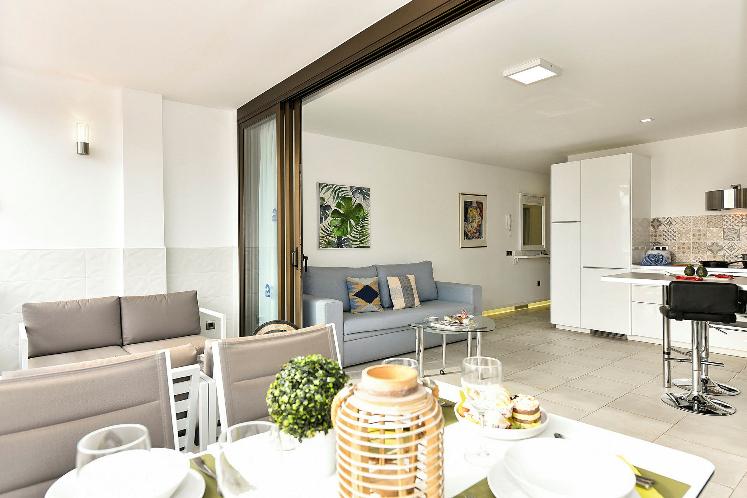 En moderne stue med åbent plan og køkken, synligt fra en terrasse med spiseområde. (AI-genereret tekst)
