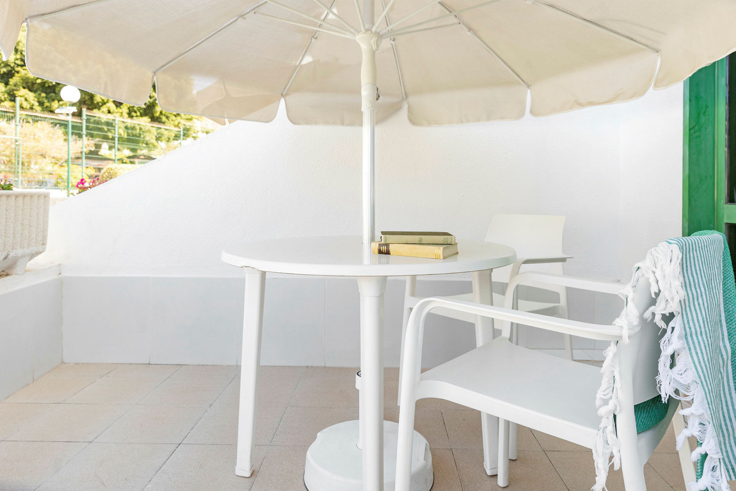 En terrasse med hvidt bord og stole, en parasol og et tæppe på en stol. (AI-genereret tekst)