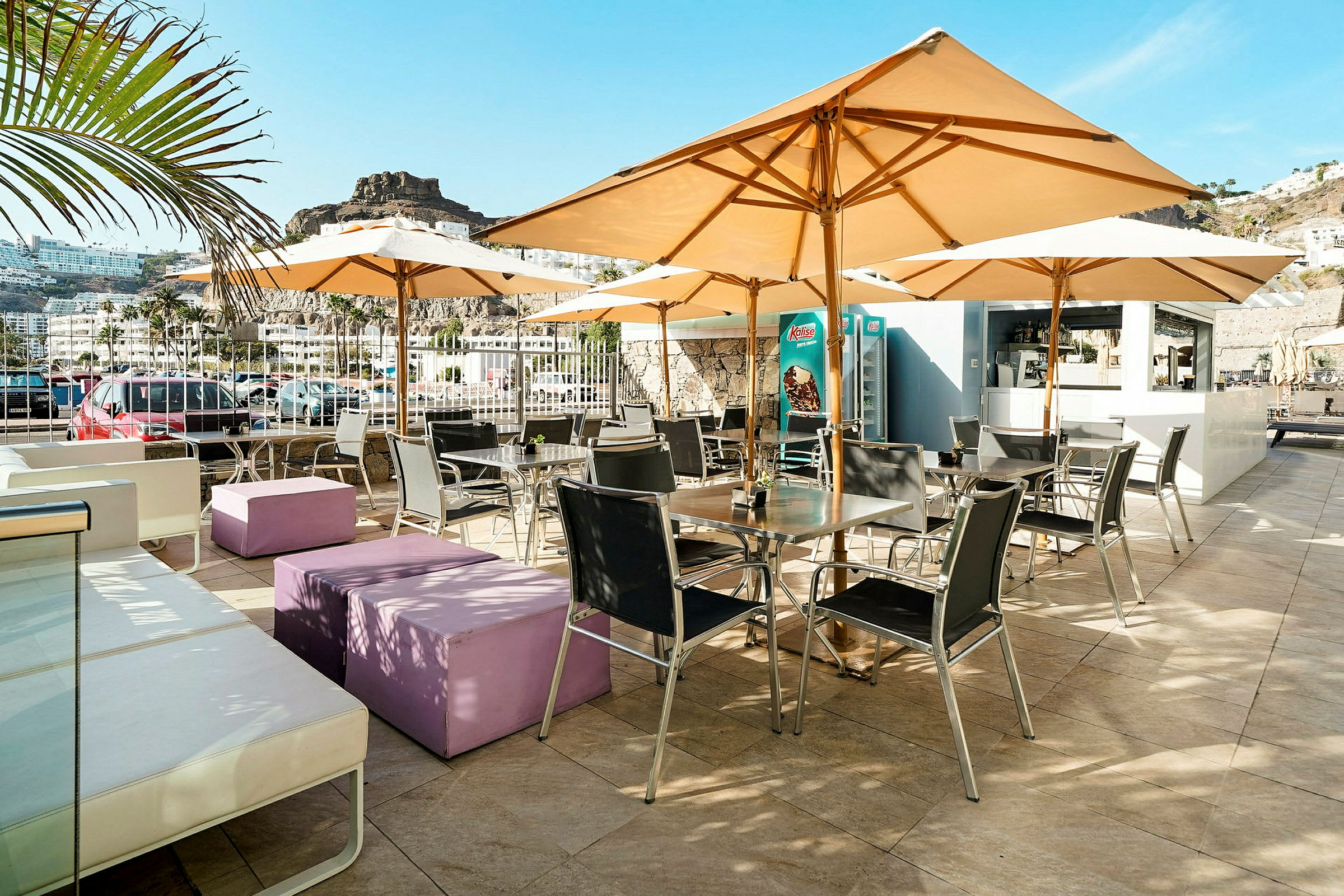 Udendørs terrasse med borde, stole og parasoller, omgivet af bjerglandskab. (AI-genereret tekst)