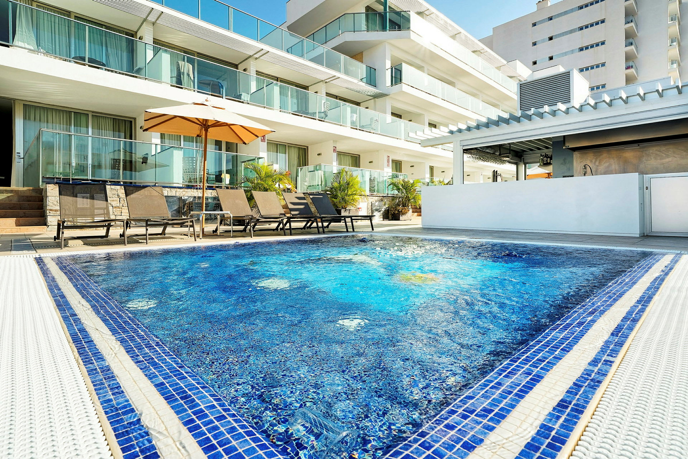 Udendørs pool med liggestole og parasol ved hotelområde. (AI-genereret tekst)