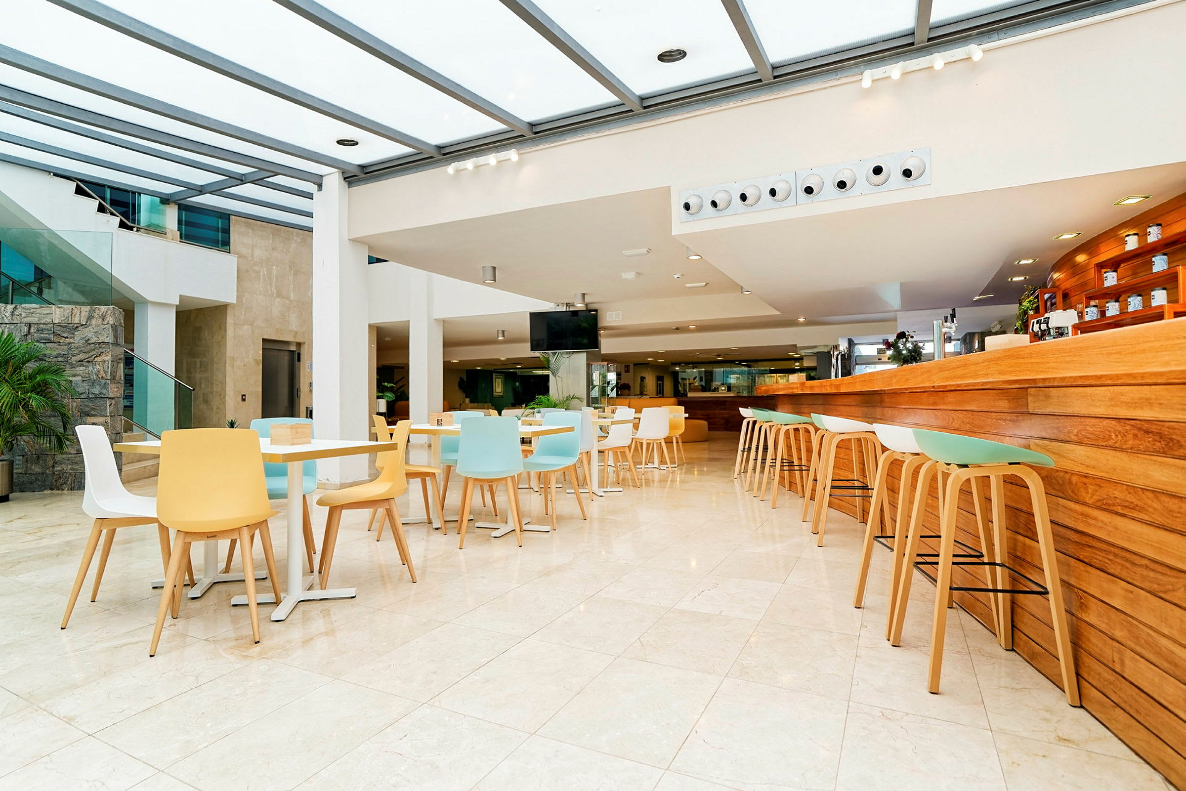 Lyst og moderne café med farverige stole og et serveringsområde med træpaneler. (AI-genereret tekst)