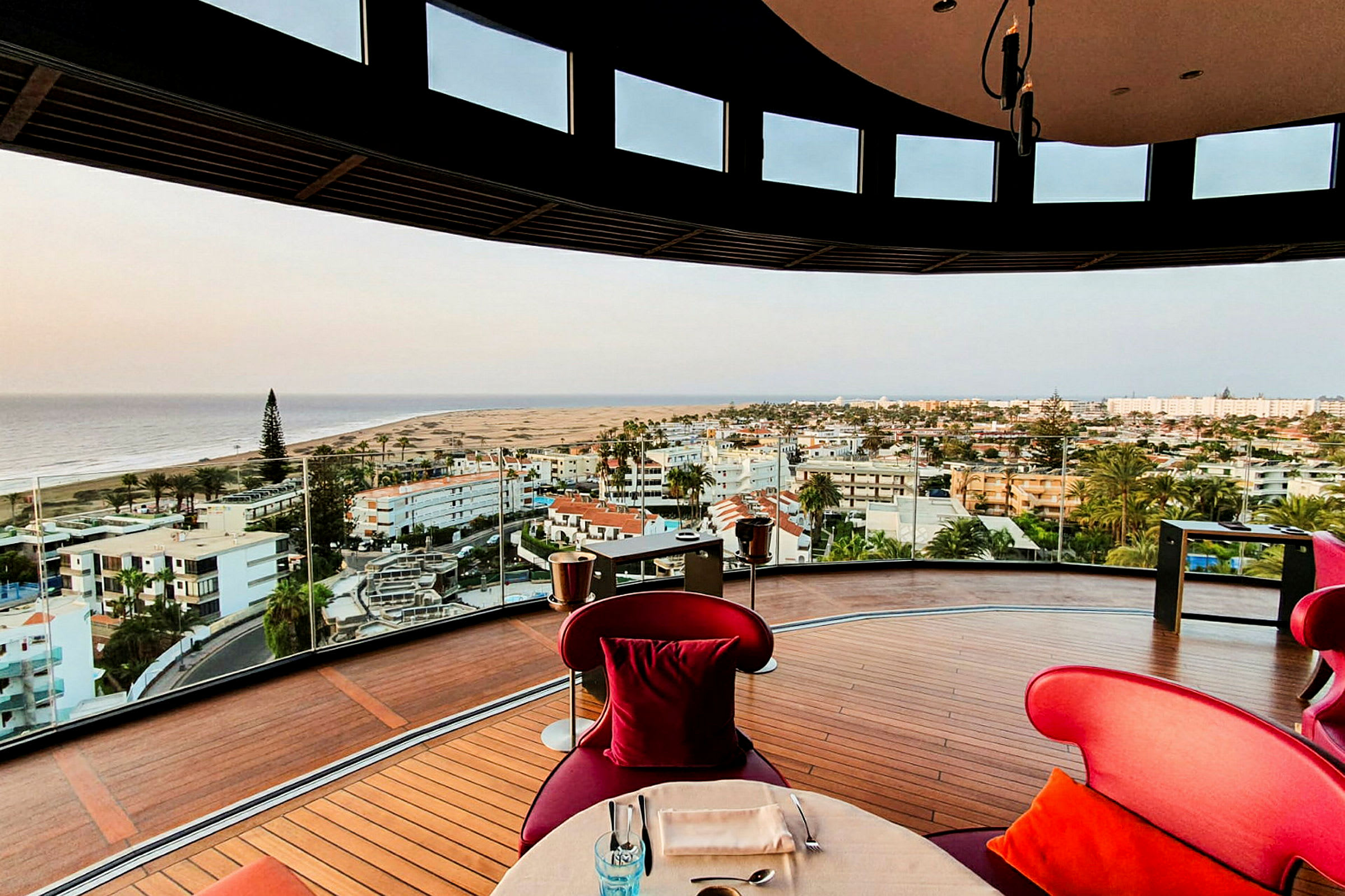 En moderne restaurant med glasvægge tilbyder panoramaudsigt over kystbyen og havet. (AI-genereret tekst)