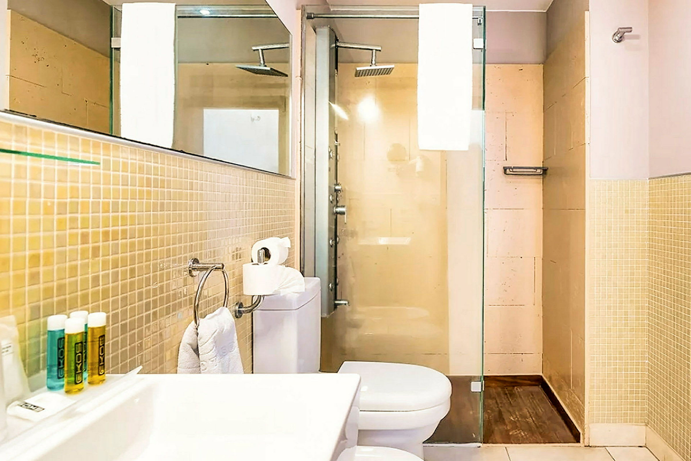 Billede af et badeværelse med bruser, toilet og håndvask. Beige vægge og glasdør til brusenichen. (AI-genereret tekst)