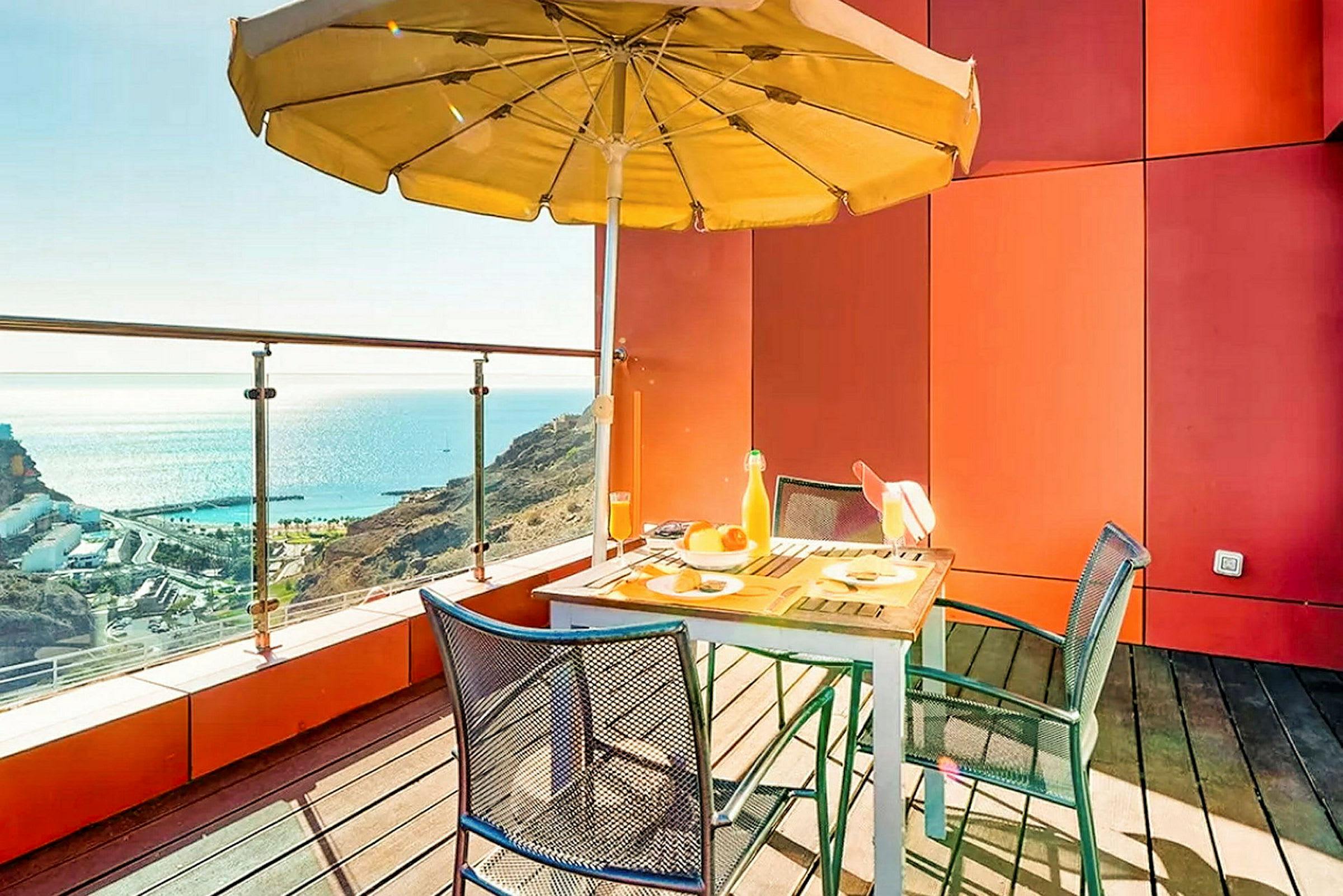 En terrasse med bord, stole og parasol med udsigt over havet. (AI-genereret tekst)