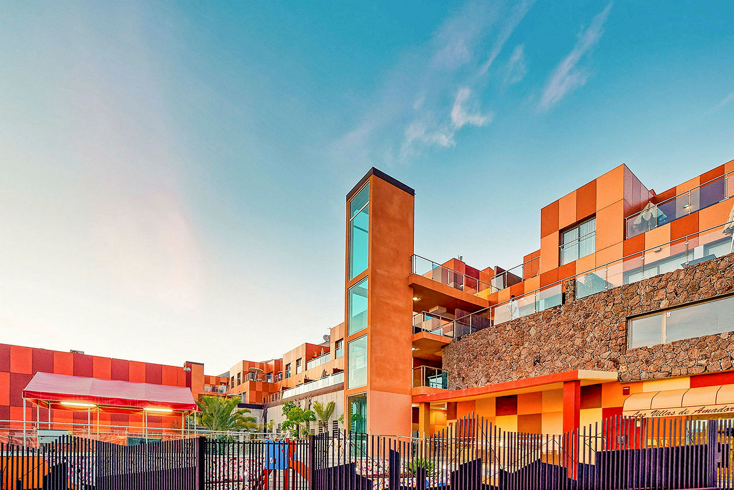 En bygning med moderne arkitektur og varme farver mod en klar blå himmel. (AI-genereret tekst)