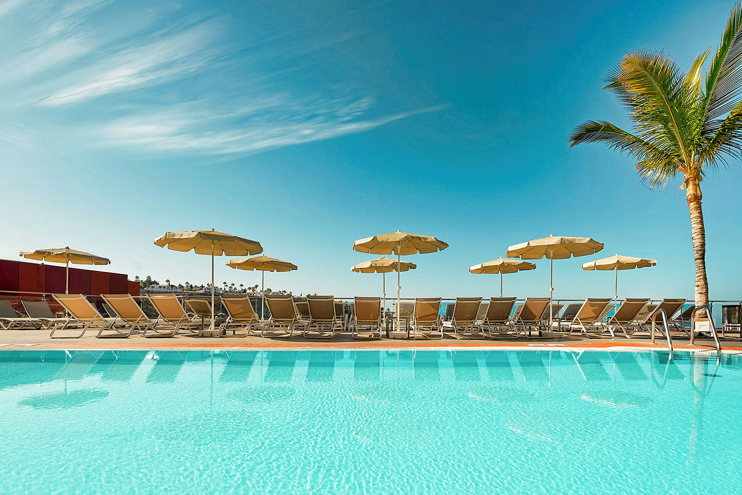 En pool med liggestole og parasoller under en klar blå himmel. (AI-genereret tekst)