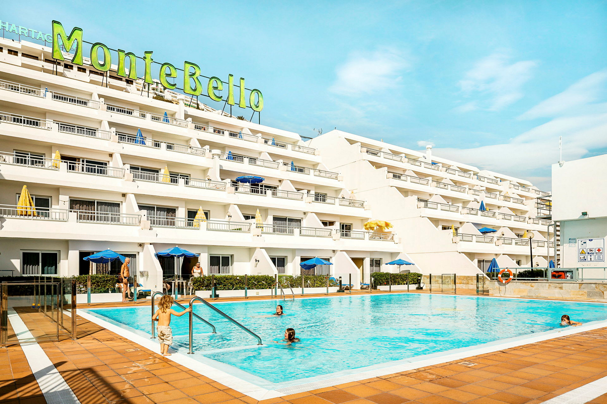 Et hotel med hvide facader og en udendørs pool foran. (AI-genereret tekst)