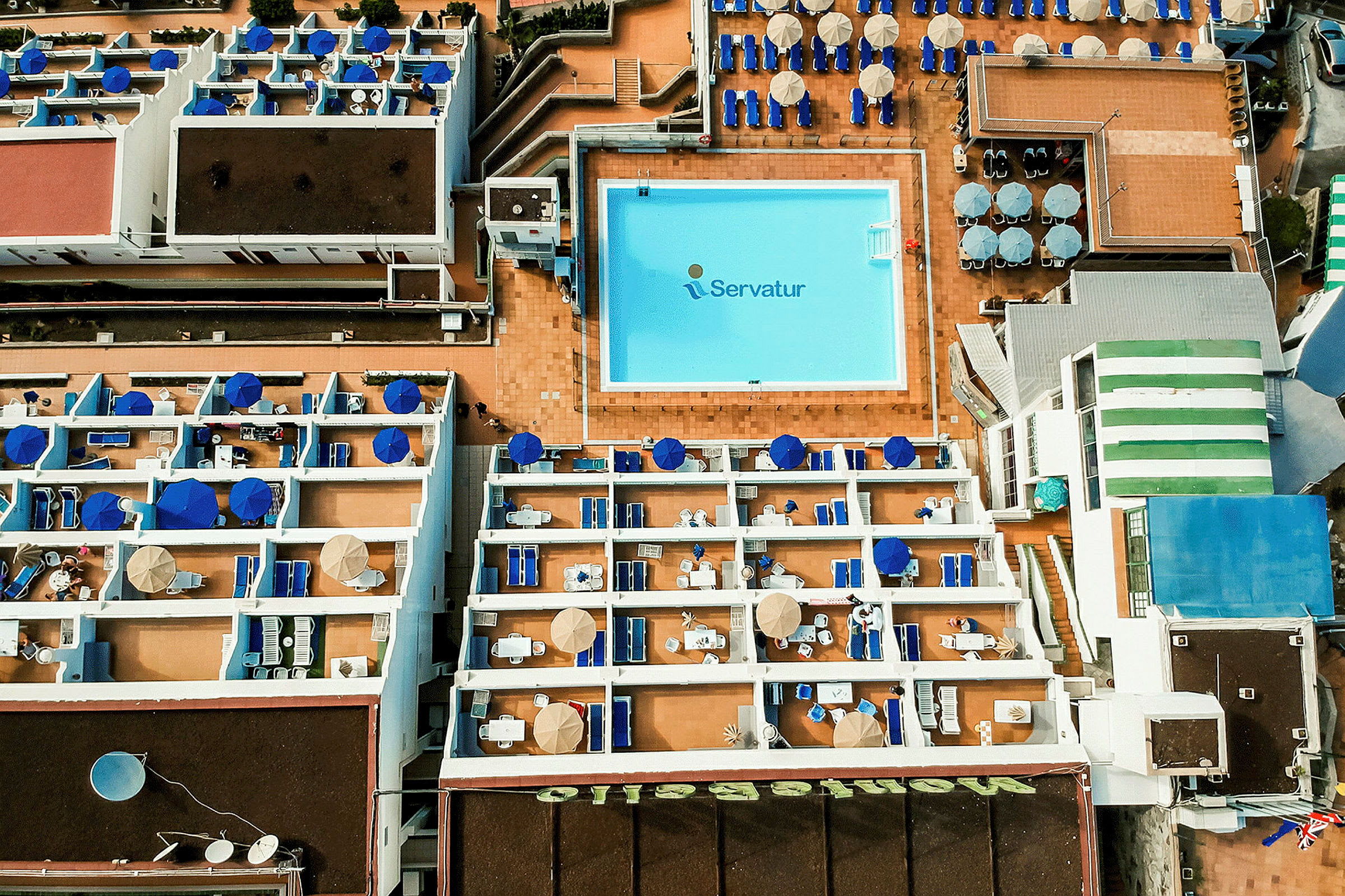 Luftfoto af hotelområde med pool og terrasser. (AI-genereret tekst)