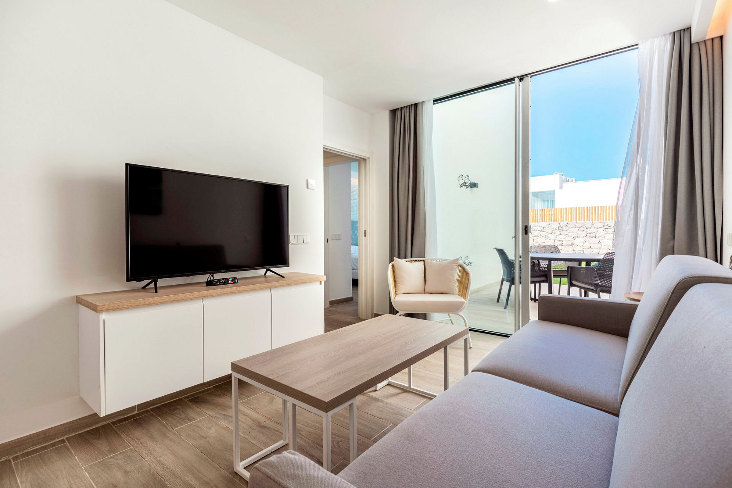 En moderne stue med sofa, sofabord, tv og vinduer, der åbner ud til en terrasse. (AI-genereret tekst)