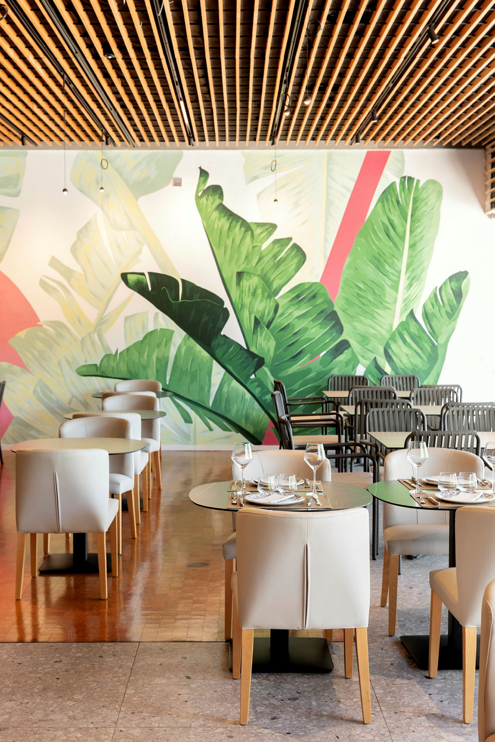Restaurantmiljø med moderne møbler og et vægmaleri af store grønne blade. (AI-genereret tekst)