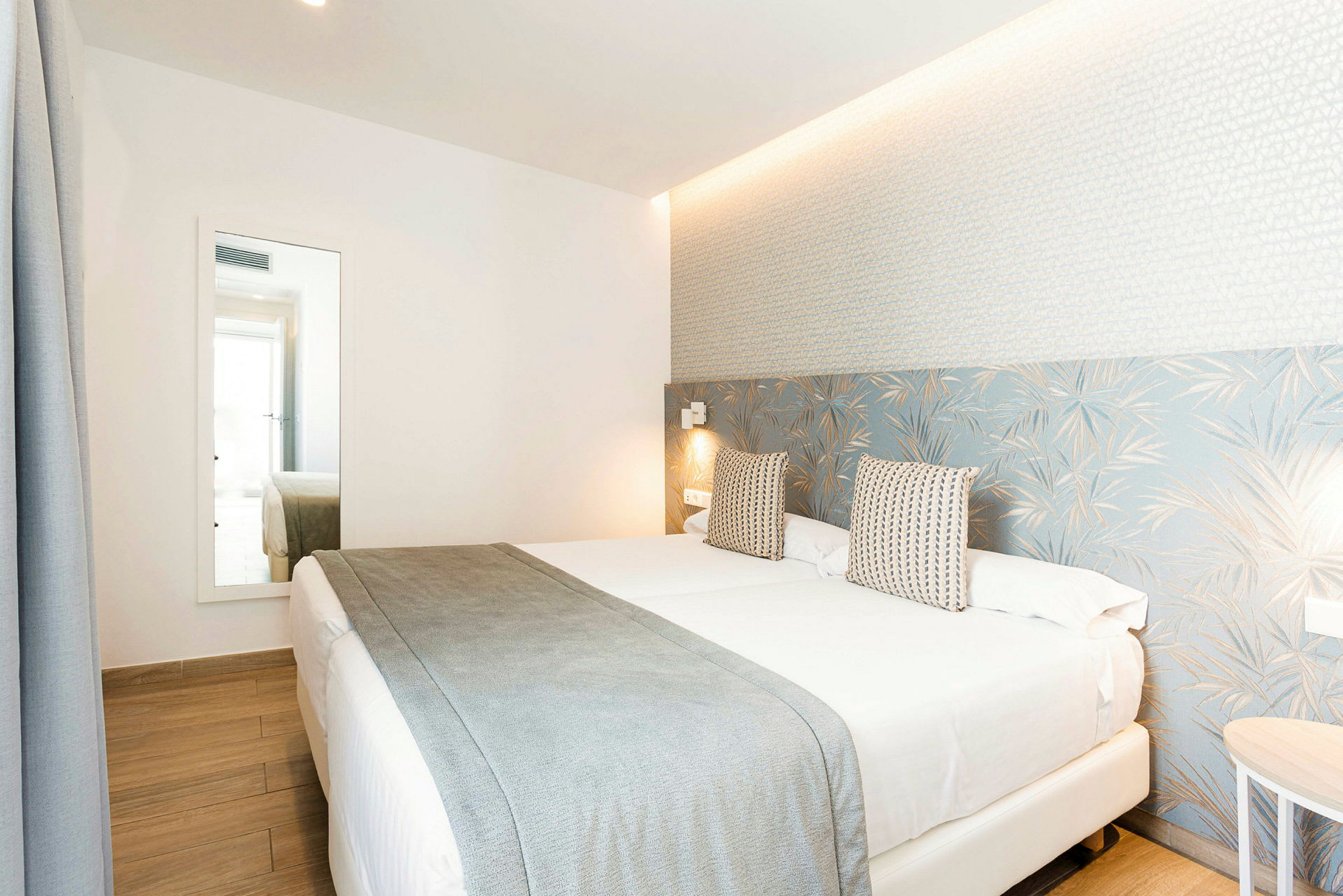 Hotelværelse med en dobbeltseng, lys indretning og et stort spejl. (AI-genereret tekst)