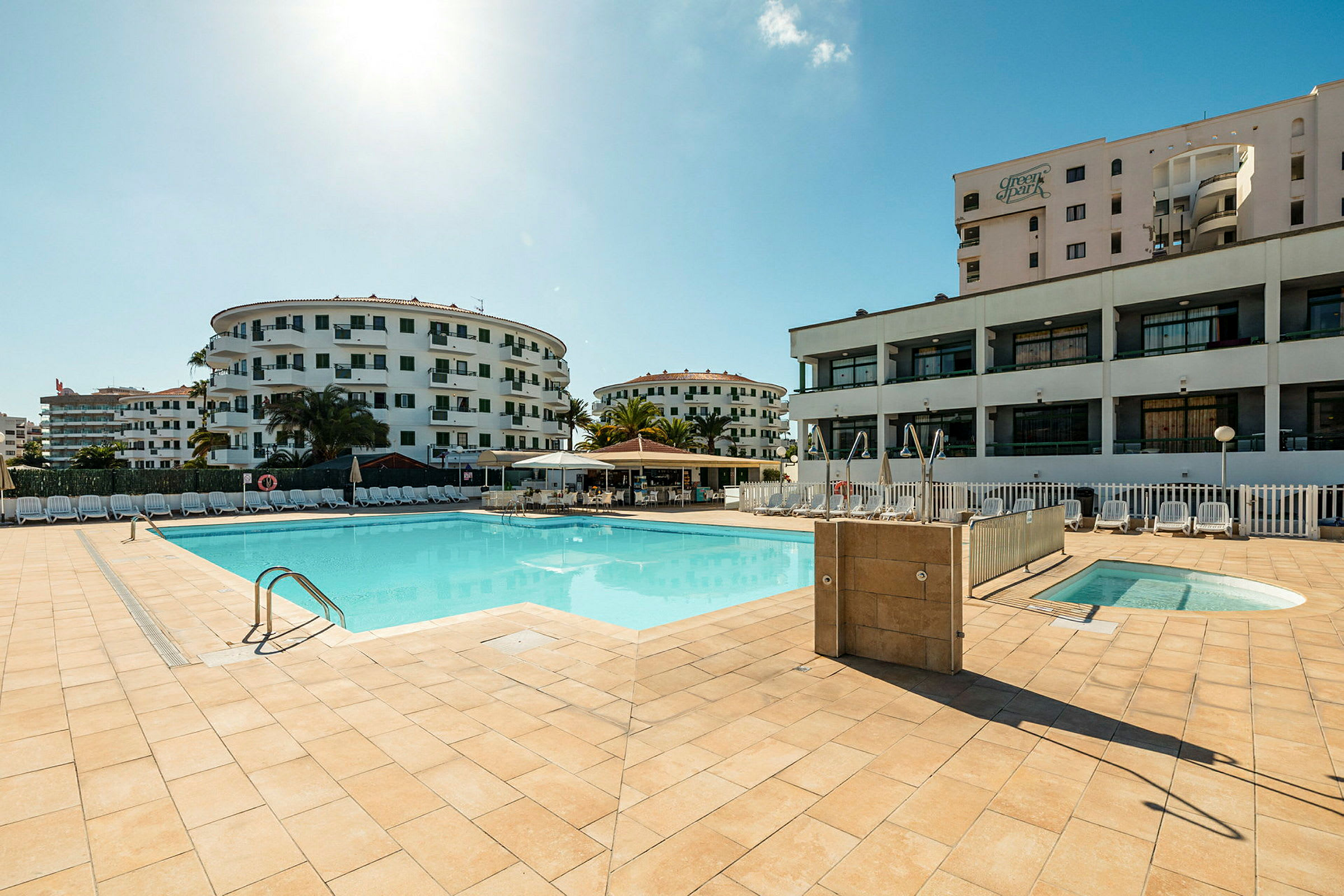 En pool med omkringliggende hotelbygninger og solsenge. (AI-genereret tekst)