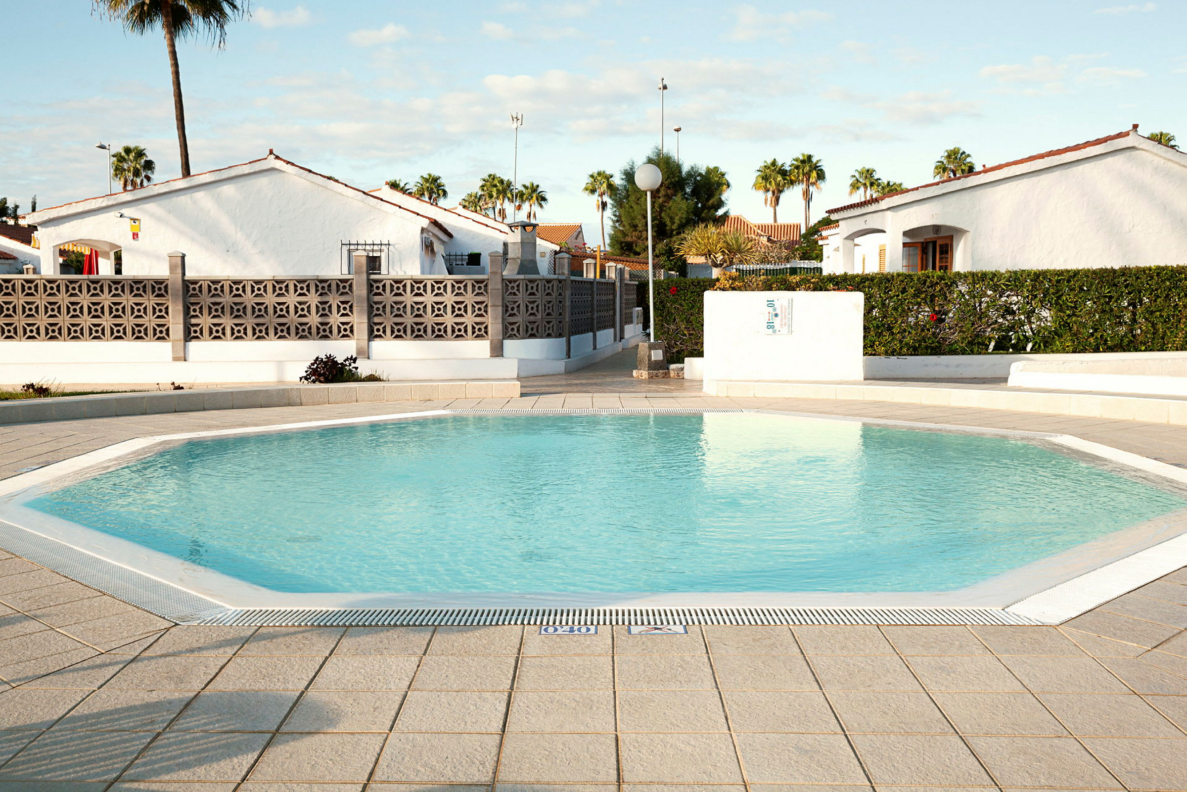 Udendørs pool ved et ferieanlæg med hvide bungalows og grønne omgivelser i baggrunden. (AI-genereret tekst)