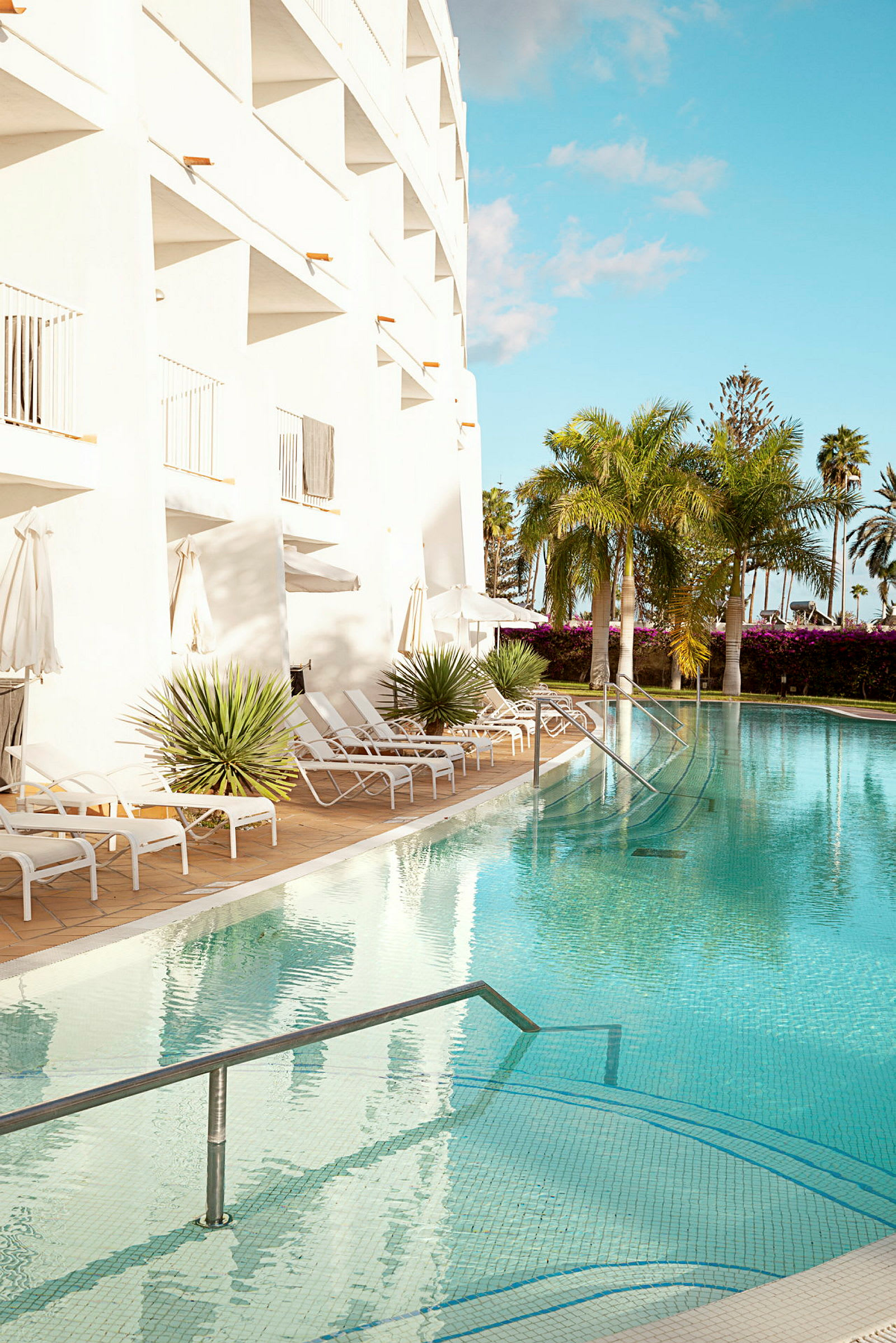Udendørs pool ved hotel med liggestole og palmer. (AI-genereret tekst)