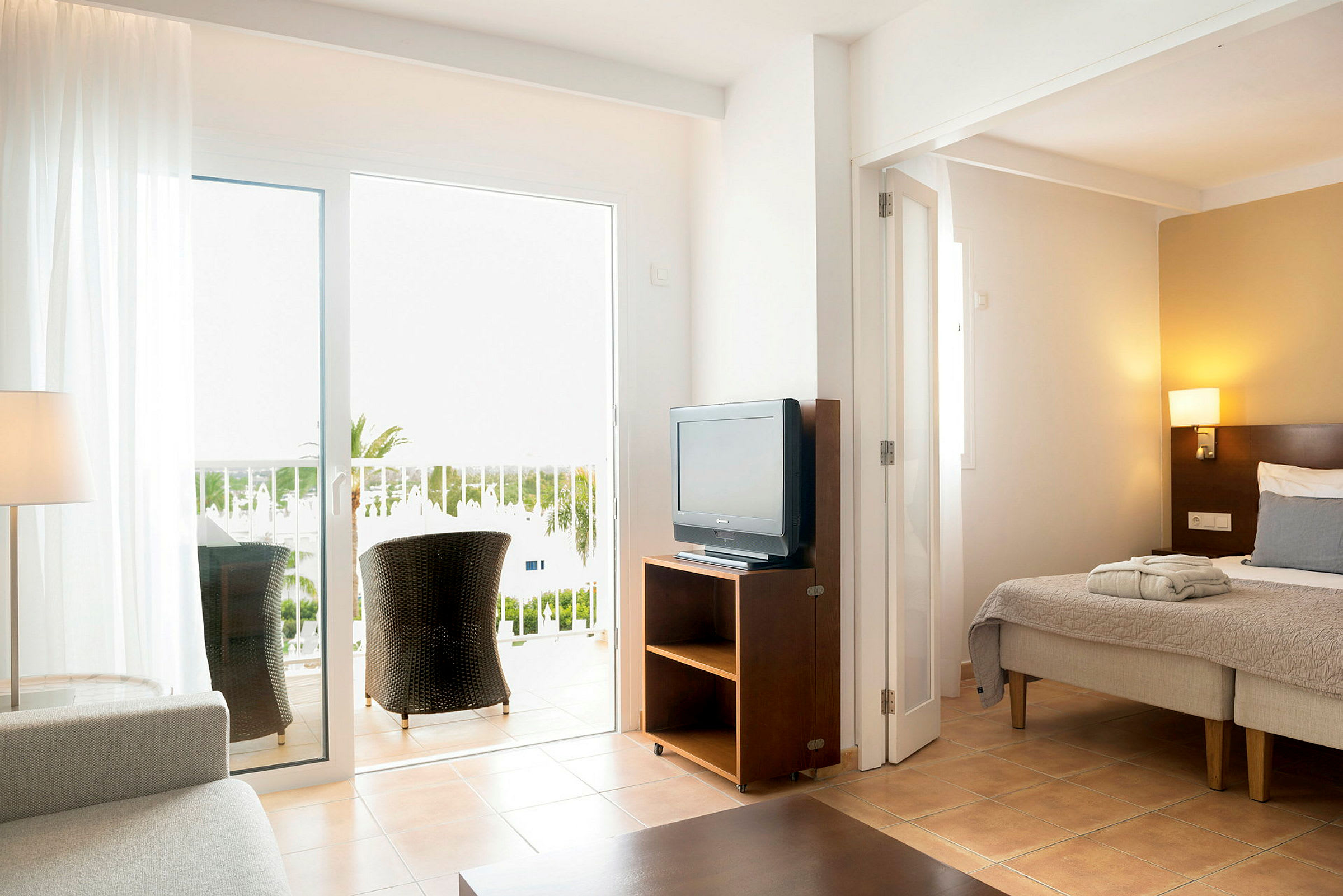 Et hotelværelse med seng, TV og balkon med siddepladser. (AI-genereret tekst)
