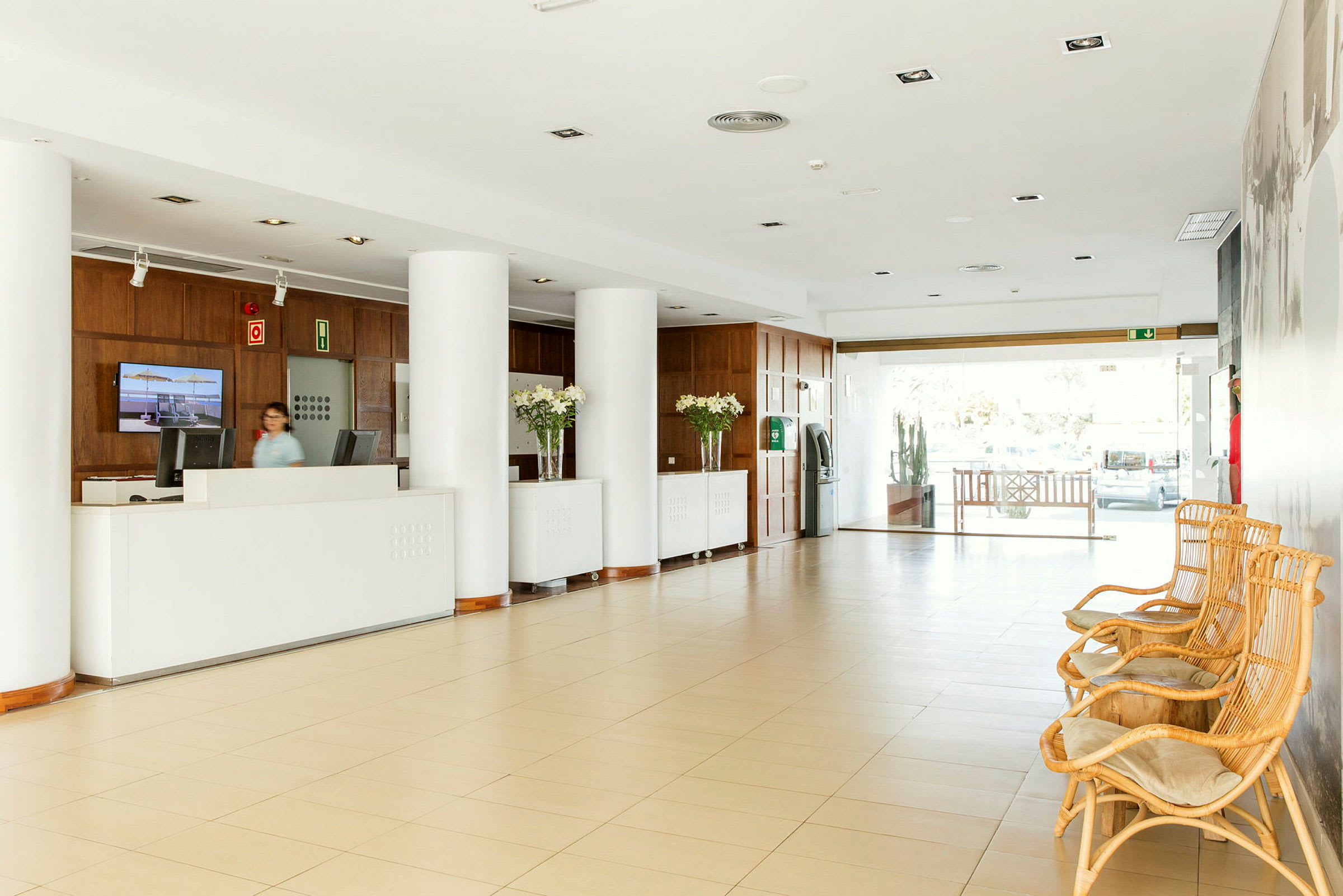 Hotellets lobby med reception, store søjler og rottingmøbler. (AI-genereret tekst)