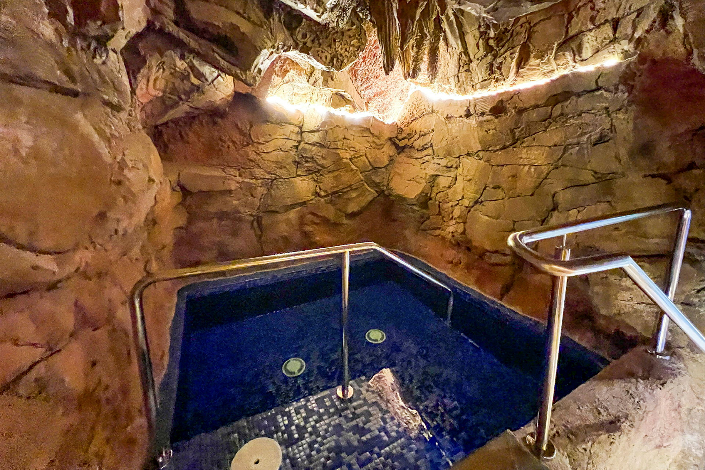 En jacuzzi omgivet af naturlignende sten vægge, med belysning langs loftet. (AI-genereret tekst)