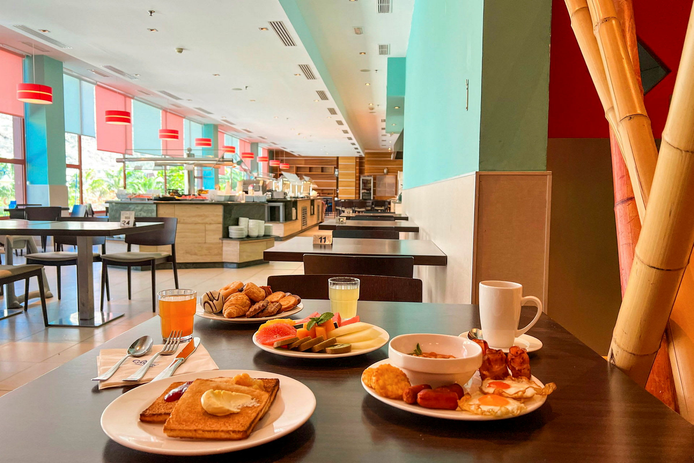 Billede af en spiseområde med flere borde og en morgenbuffet i baggrunden. På et bord i forgrunden står tallerkener med forskellige morgenmadsmuligheder. (AI-genereret tekst)
