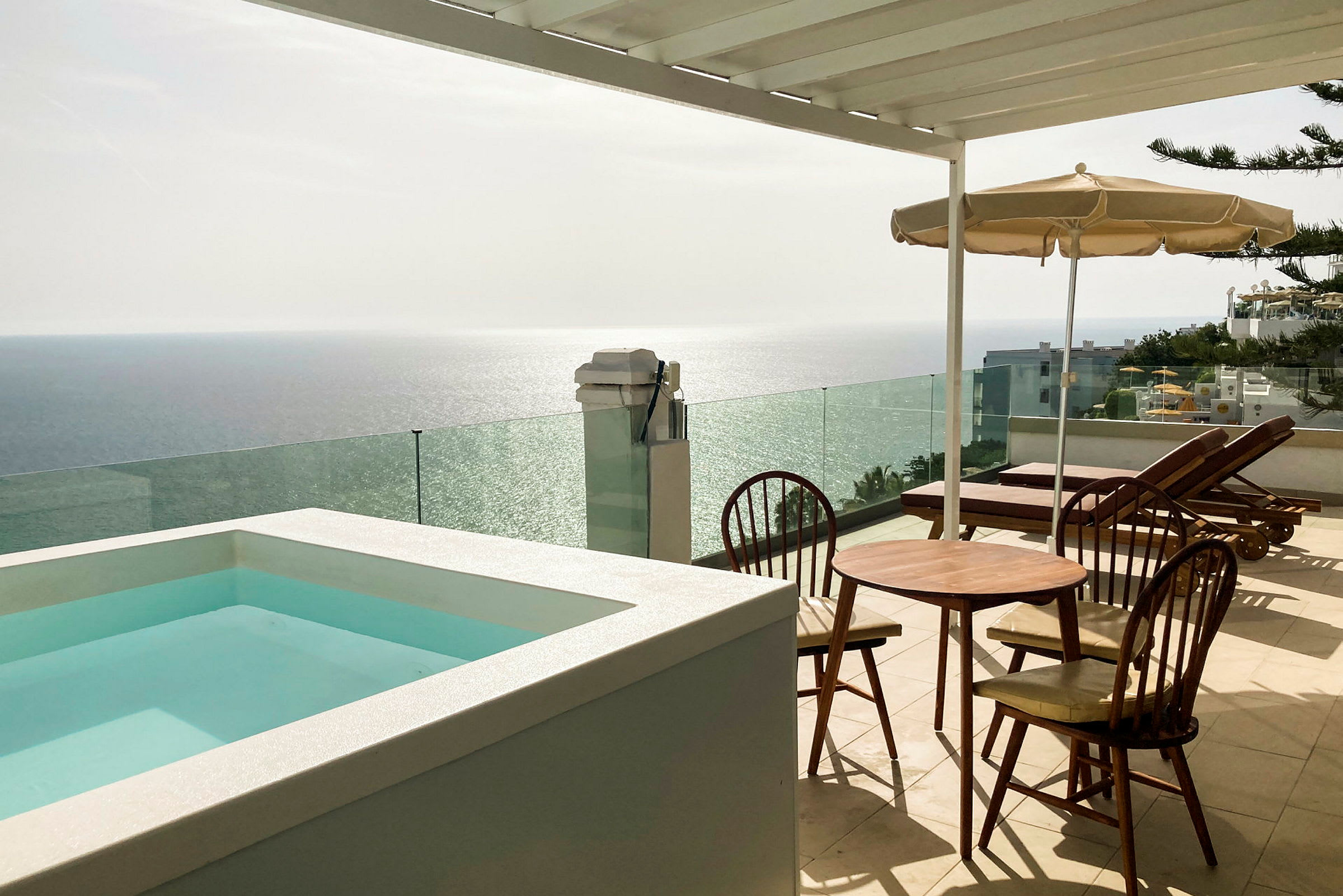 Terrasse med en lille pool, bord og stole samt liggestole med udsigt over havet. (AI-genereret tekst)